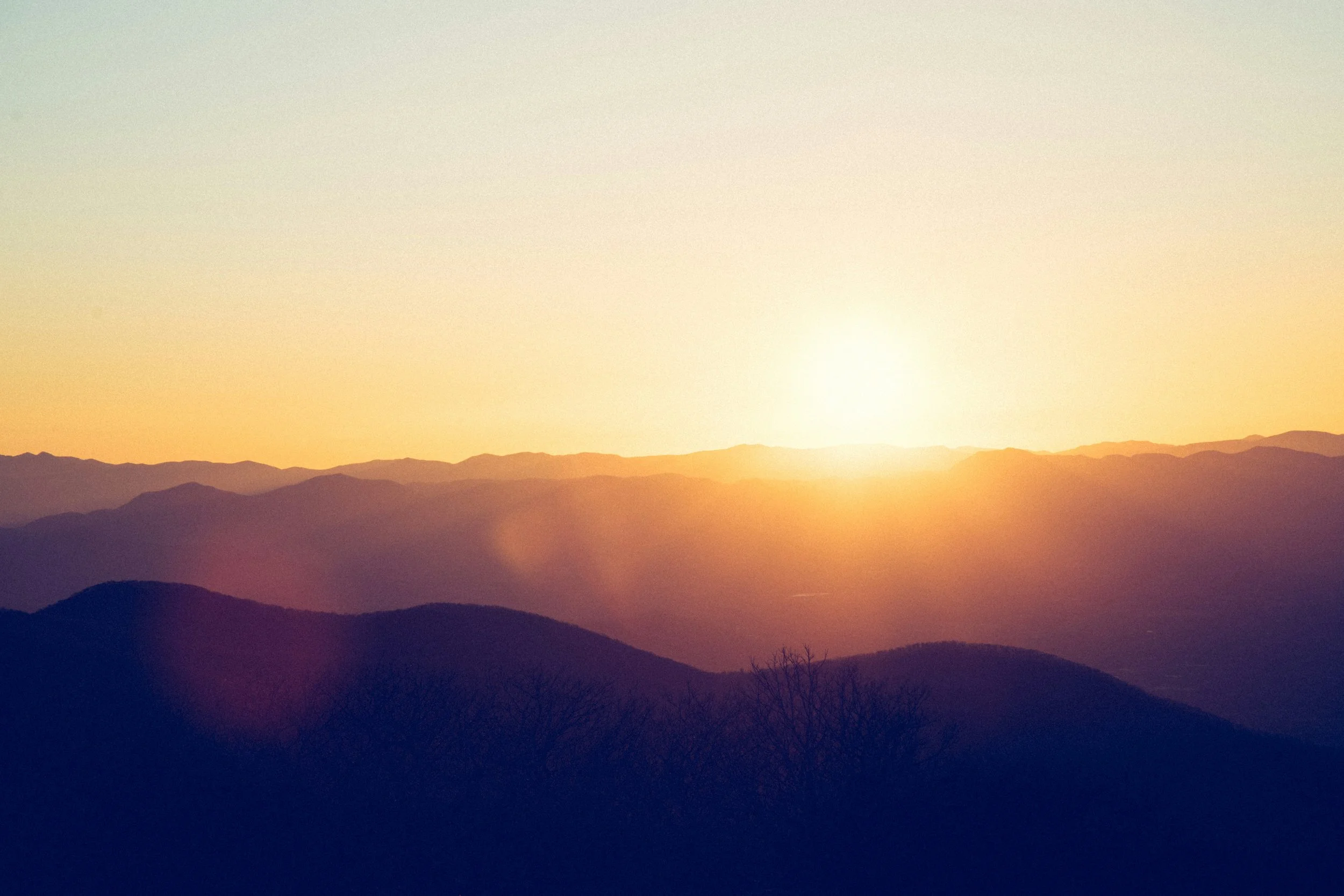 Coucher de soleil derrière une chaîne de montagnes, avec un ciel clair et doux.
