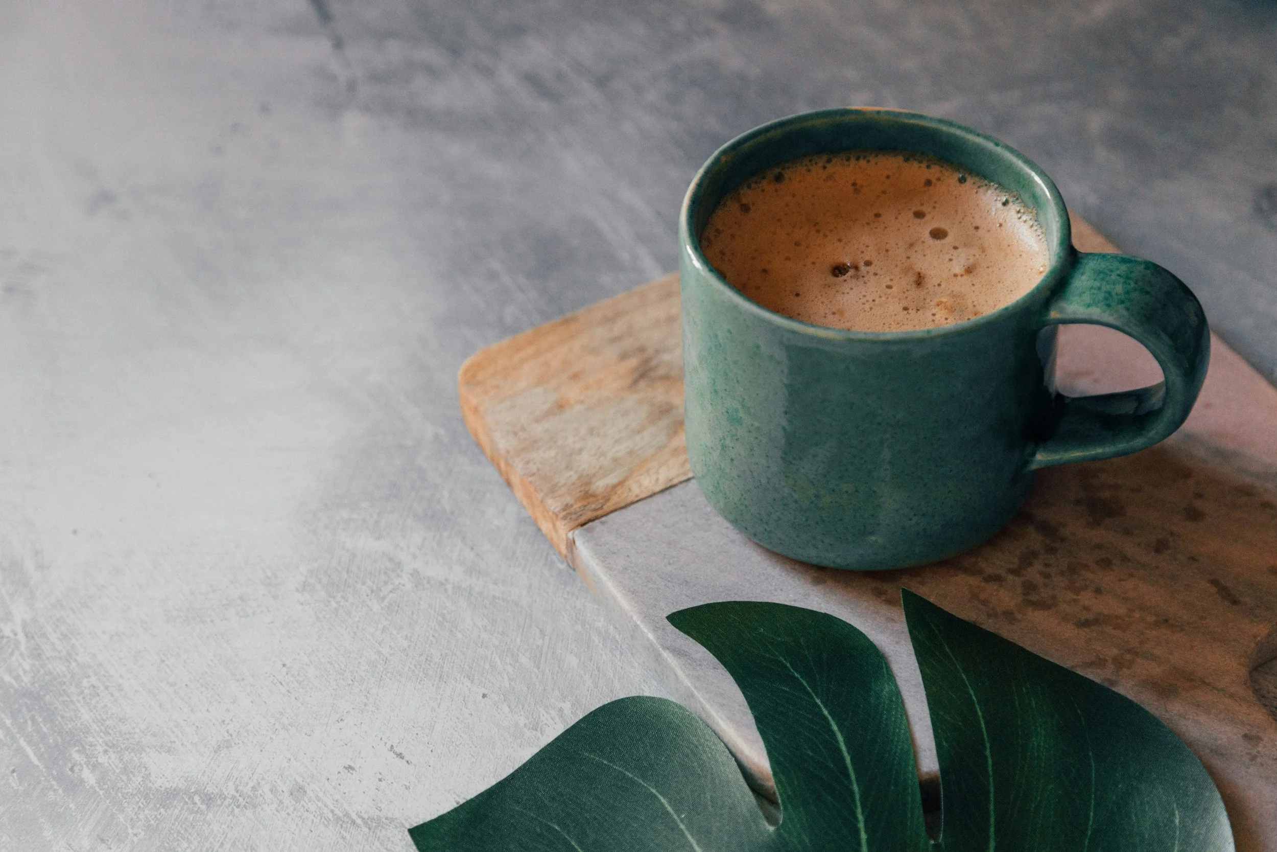 Tasse en céramique verte contenant une boisson chocolatée, placée sur une planche en bois sur une surface en pierre