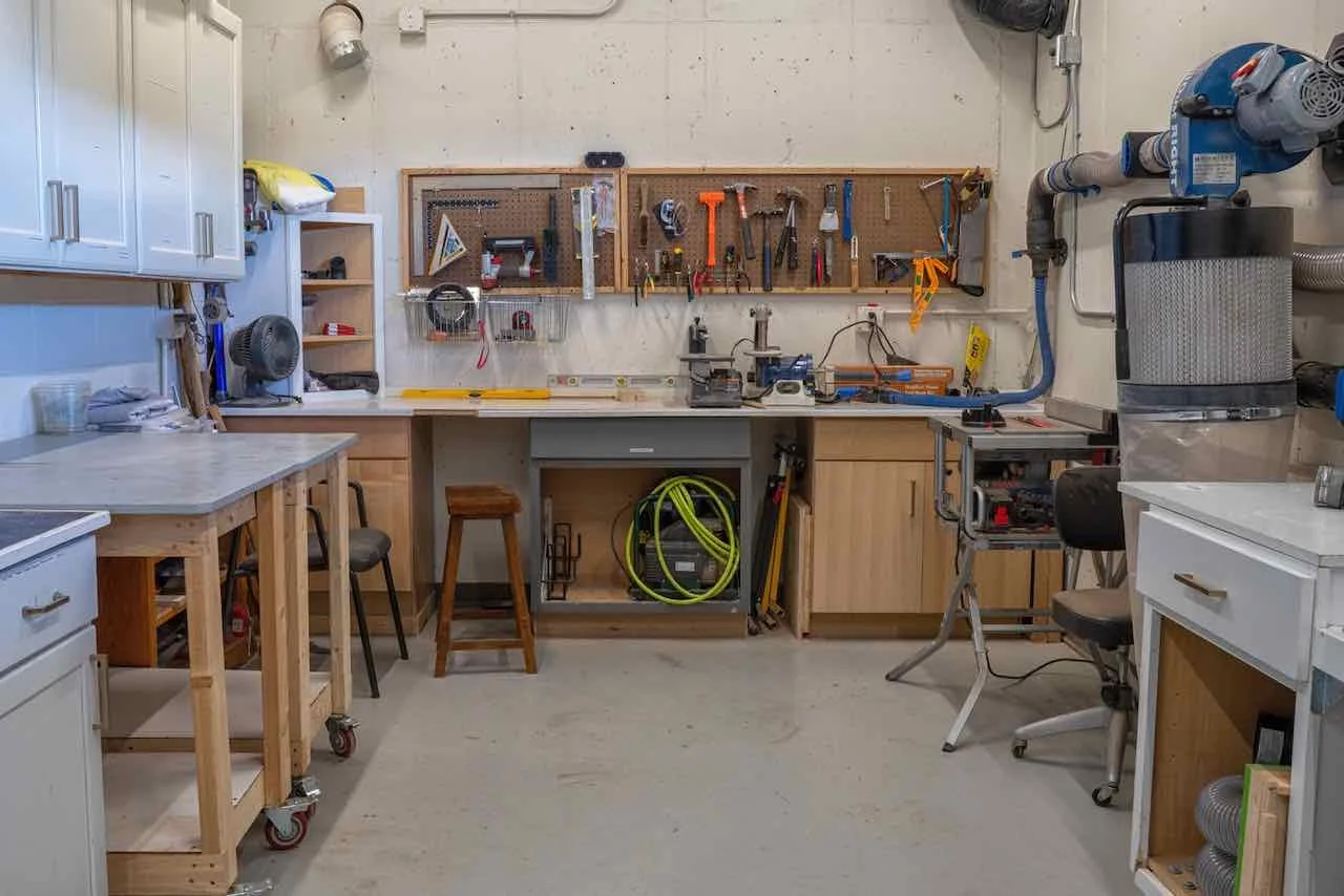 A well-organized woodworking workshop with tools hanging on a pegboard, workbenches with chairs, storage cabinets, and equipment for project work.