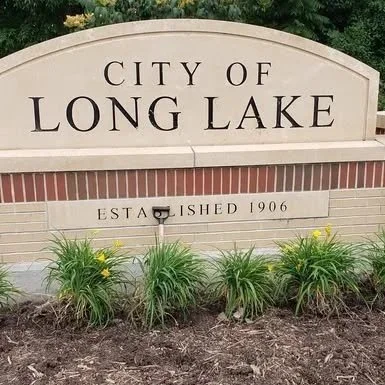Sign for the city of Long Lake, established in 1906, with shrubs and flowers in front of it.