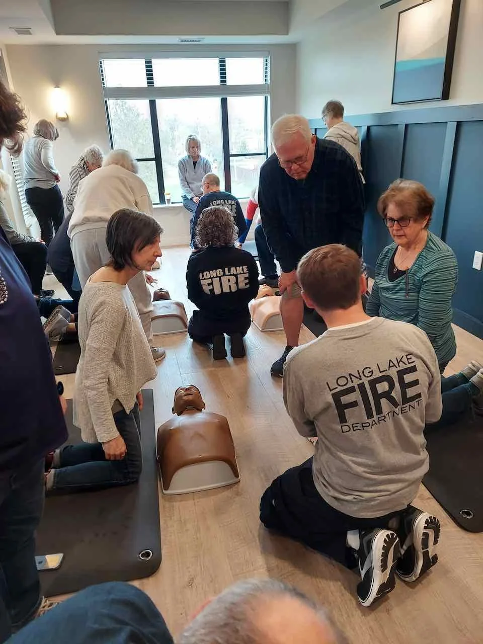 People participating in a CPR training class with mannequins on the floor, led by instructors from the Long Lake Fire Department.