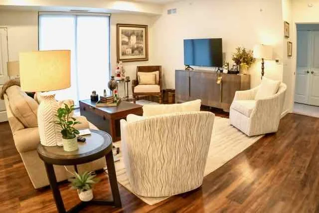 Living room with beige and white furniture, a wooden coffee table, a TV on a gray cabinet, and sliding glass doors leading outside.