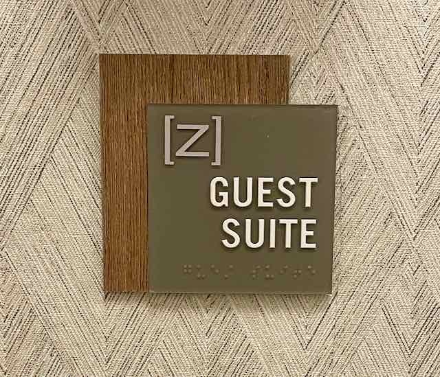 Sign indicating a guest suite, with a wood background and Braille at the bottom.