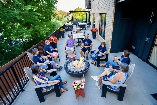 A group of people sitting around a fire pit on a balcony, enjoying drinks and conversation.