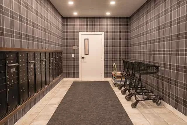 Mailboxes on the left wall, shopping carts on the right, door at the back, plaid wallpaper, tiled floor, gray rug in the center.