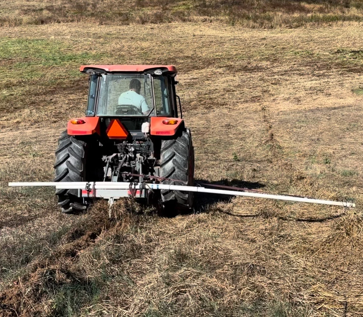 A person operating a red tractor in a field, using a wide attachment to spray or treat the land.