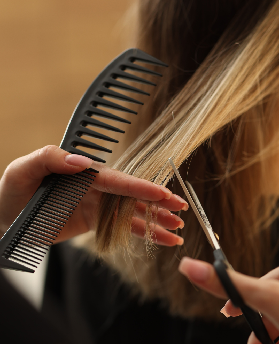 A person cutting blonde hair with scissors while holding a black comb.