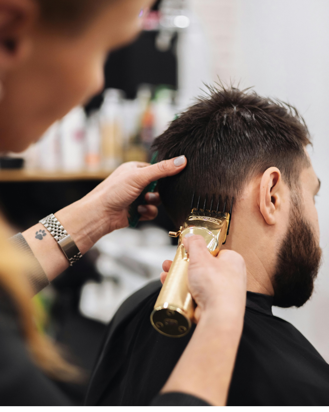Barber trimming a man's hair with electric clippers at a salon.