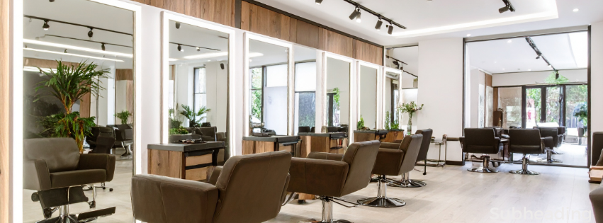 Inside a modern hair salon with multiple styling stations, mirrors, and salon chairs, some with hairdressing equipment, and large windows allowing natural light.