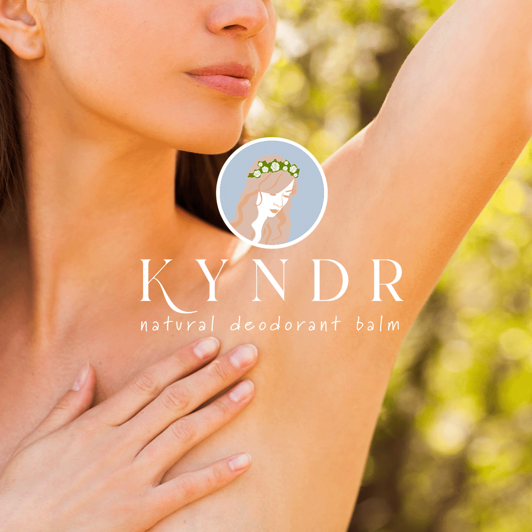 A woman with fair skin and light brown hair raising her arm in a natural outdoor setting, promoting KYNDR natural deodorant balm.