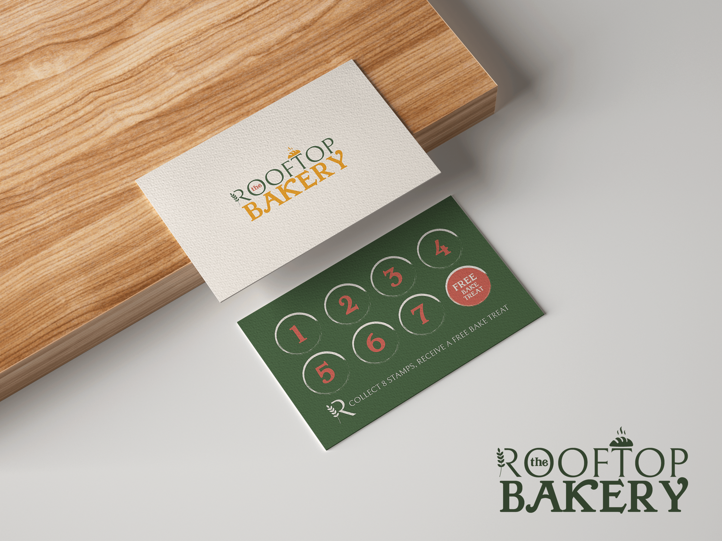 Close-up of a business card for The Roof Top Bakery on a wooden surface, and part of a green stamp card underneath.