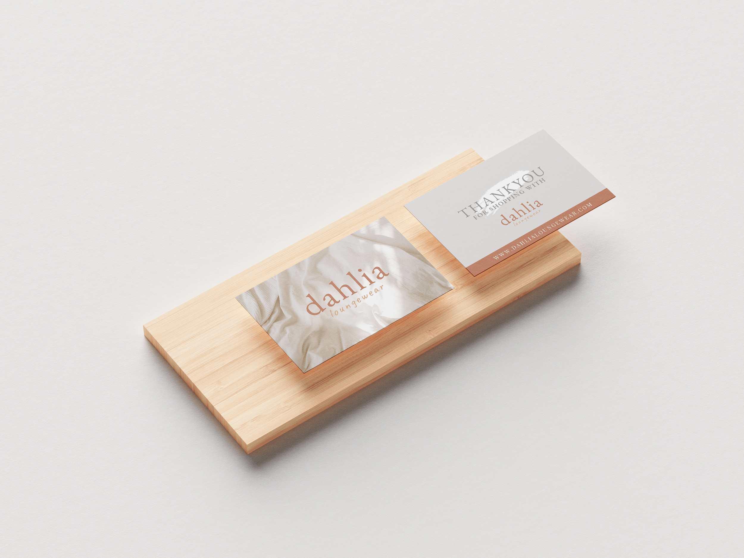 Wooden tray holding tissues and business cards with branding for Dahlia Loungewear, placed on a white surface.