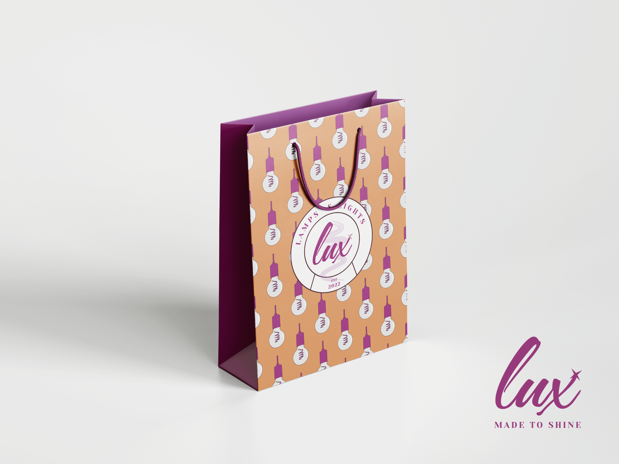 A purple and orange gift bag with a pattern of light bulbs and a circular logo labeled 'Lampsights Lux,' featuring the phrase 'Made to Shine,' placed on a white surface with a plain background.