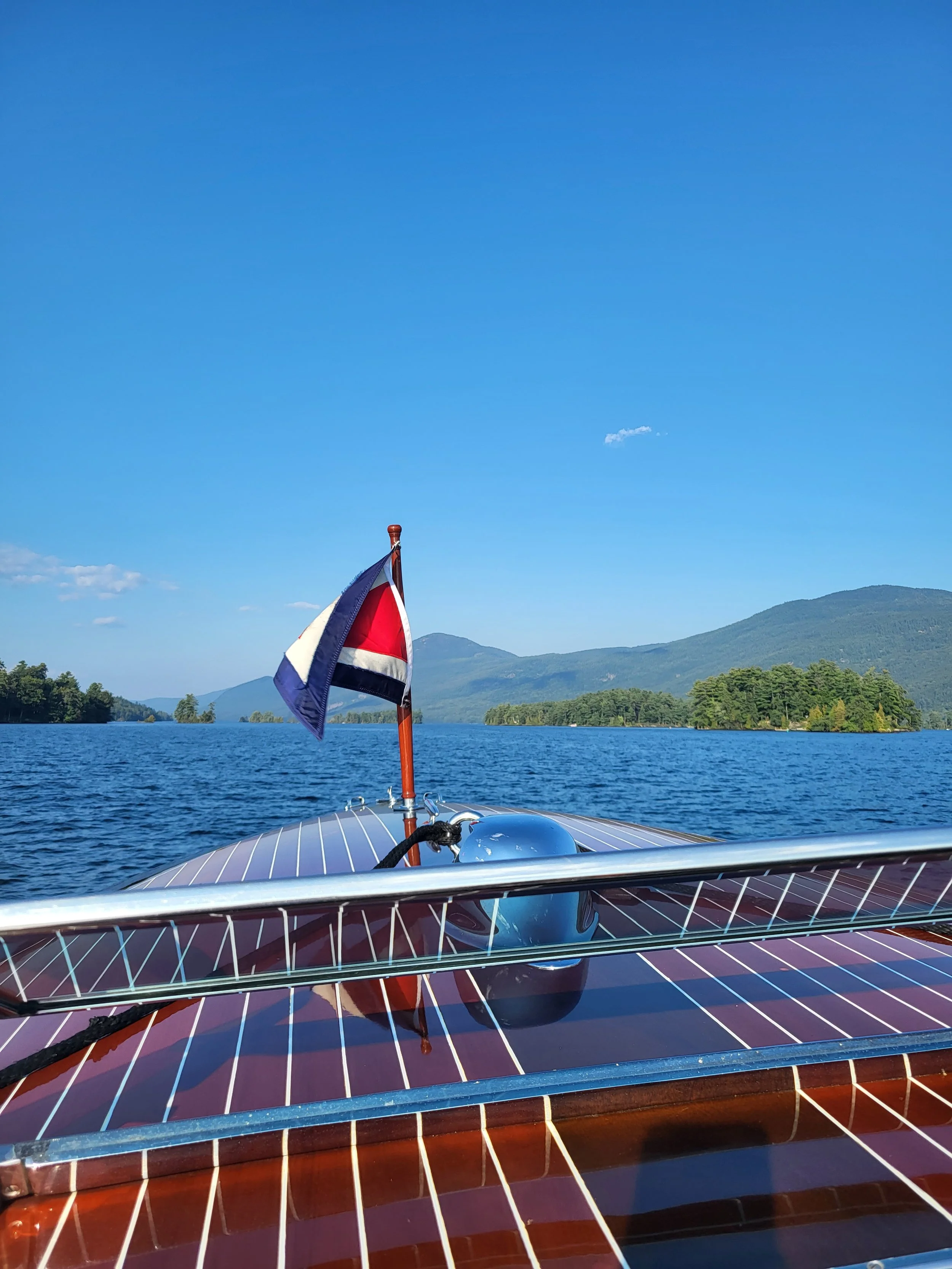 View of a boat on a lake with a flag, mountains in the background, and a clear blue sky.