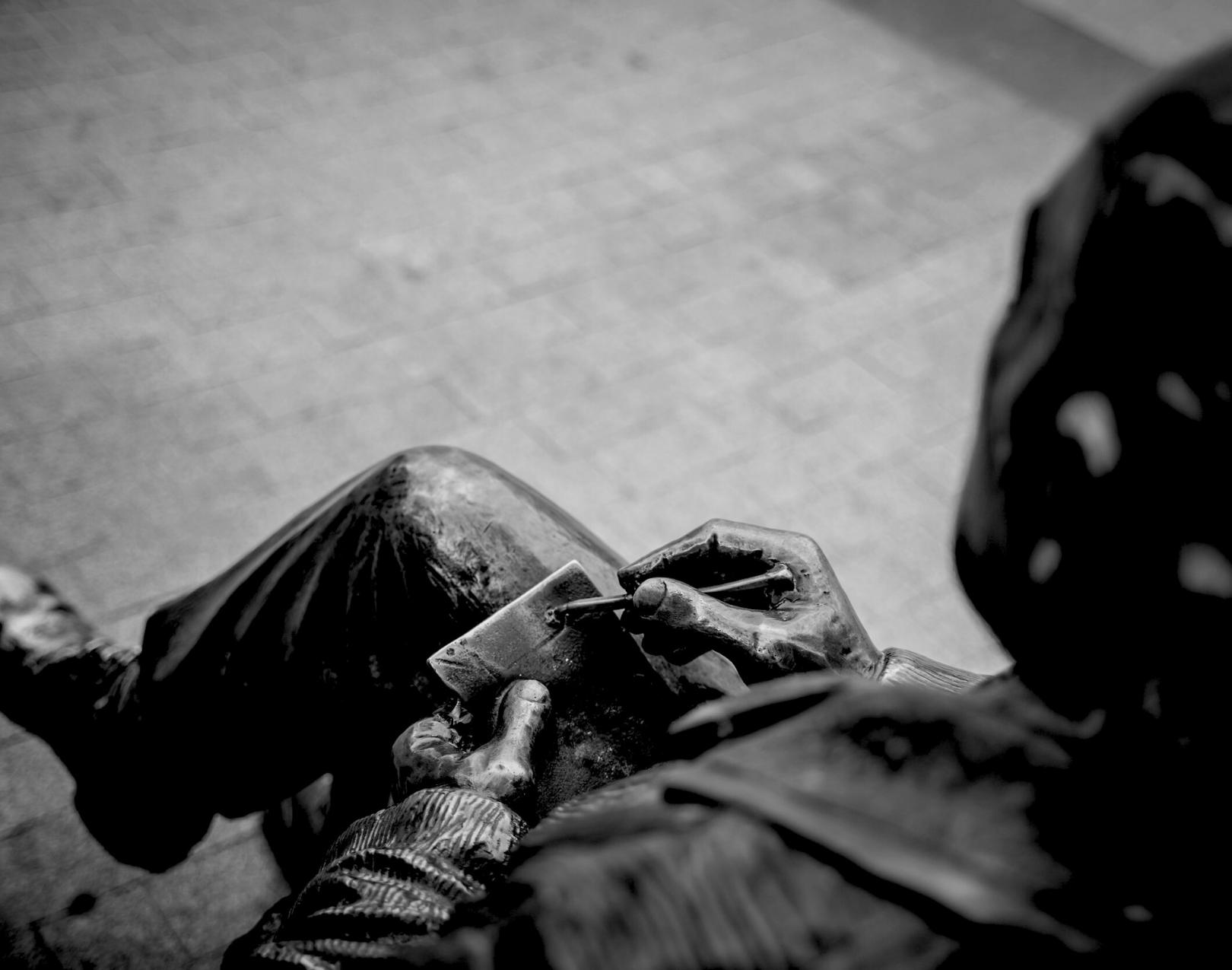 A person sitting on the ground, writing or drawing on a small rectangular surface with a thin tool, seen from above in black and white.