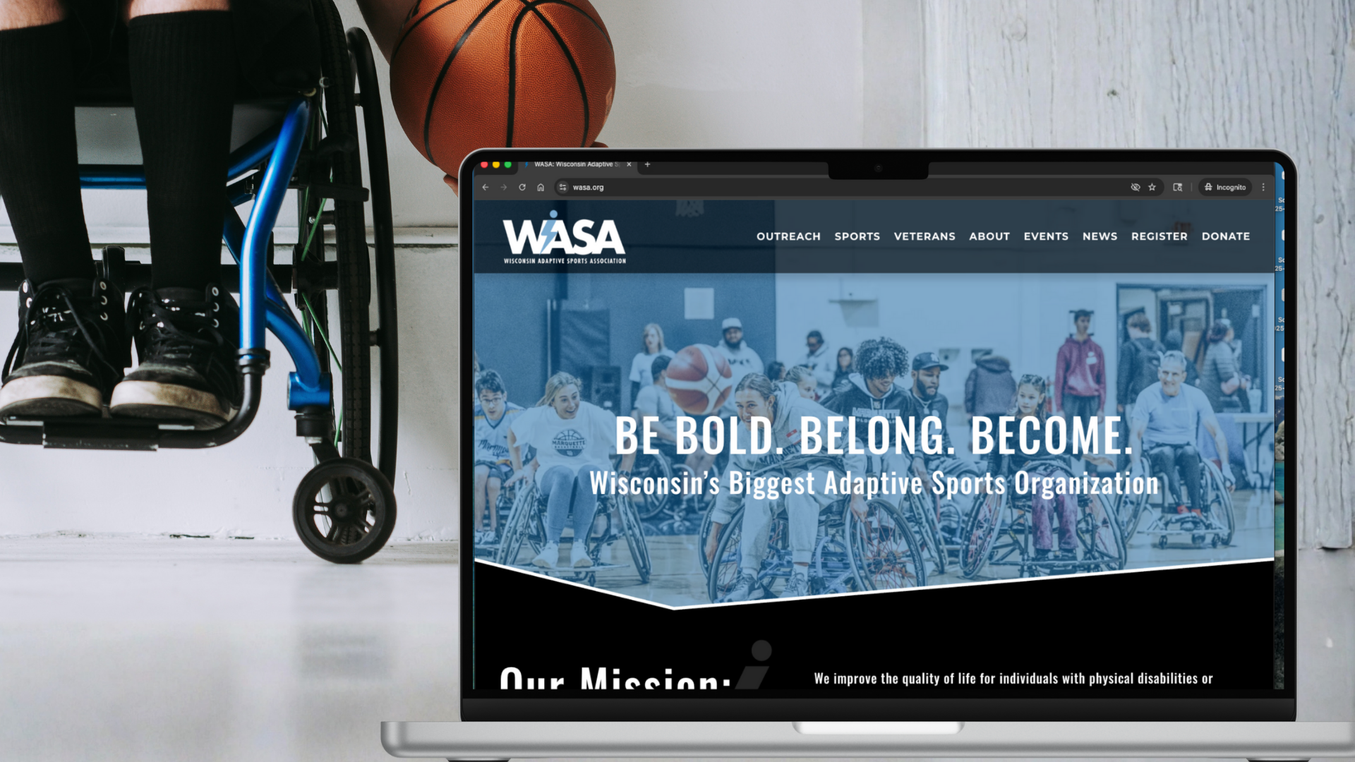 Laptop displaying the Wisconsin Adaptive Sports Association website, with a background of people in wheelchairs at a sports event, and a mobility scooter and basketball in the background.