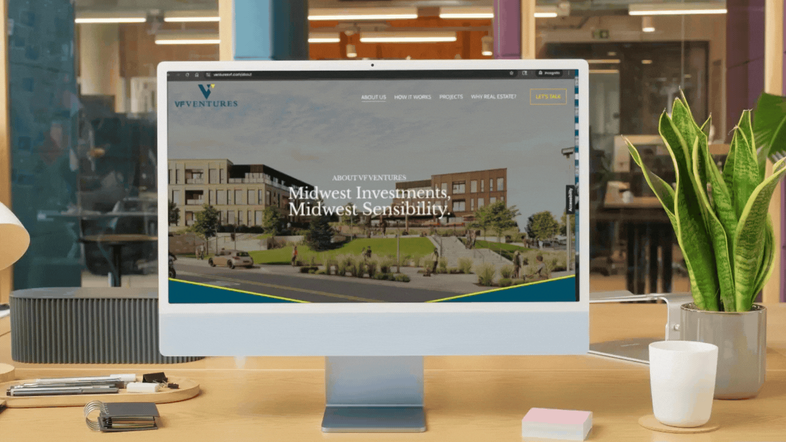 A computer monitor on a desk displaying a real estate website, with a potted plant, sticky notes, and writing utensils nearby.