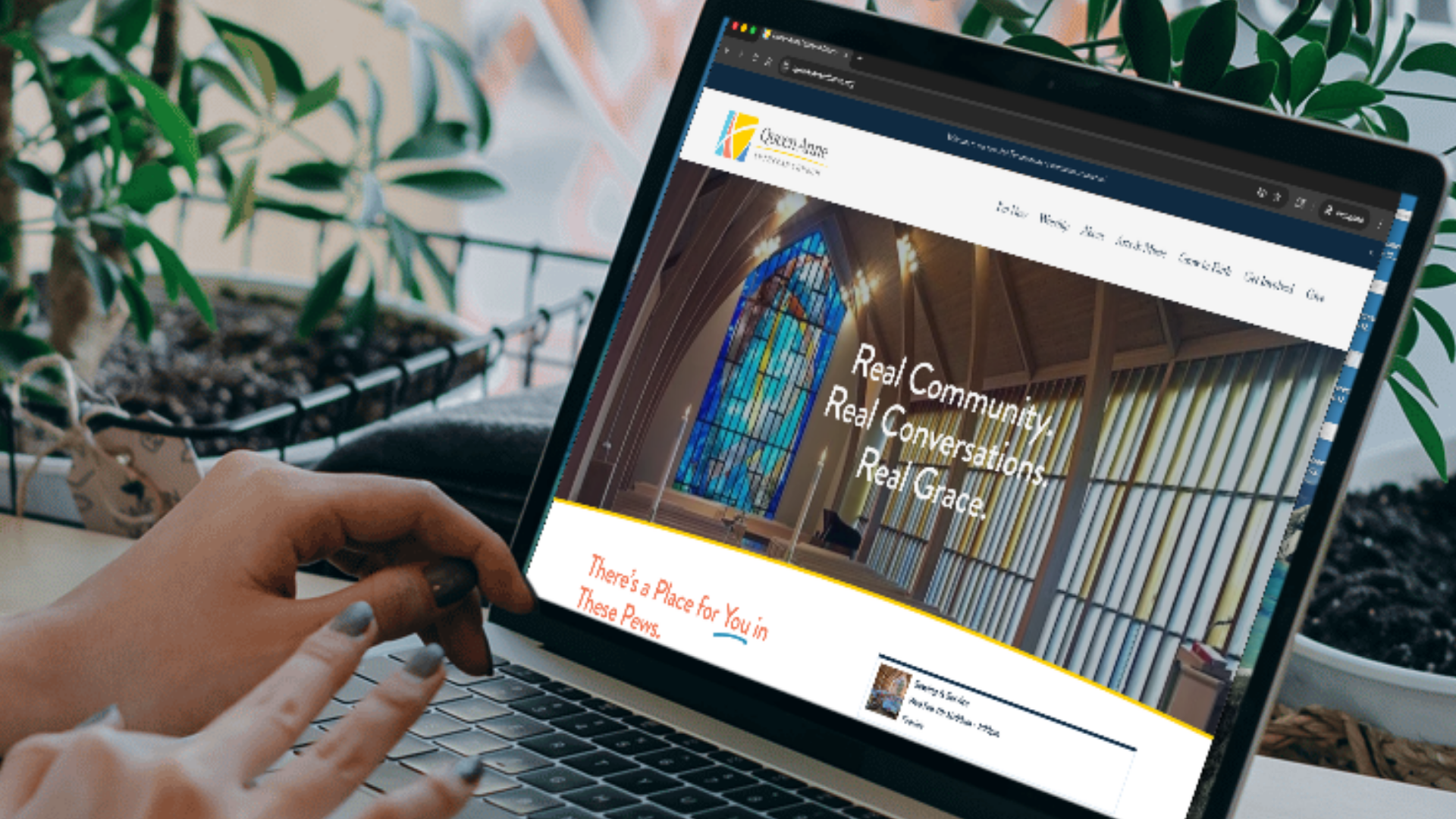 A person browsing a church's website on a laptop, showing a stained glass window and interior design, with indoor plants nearby.
