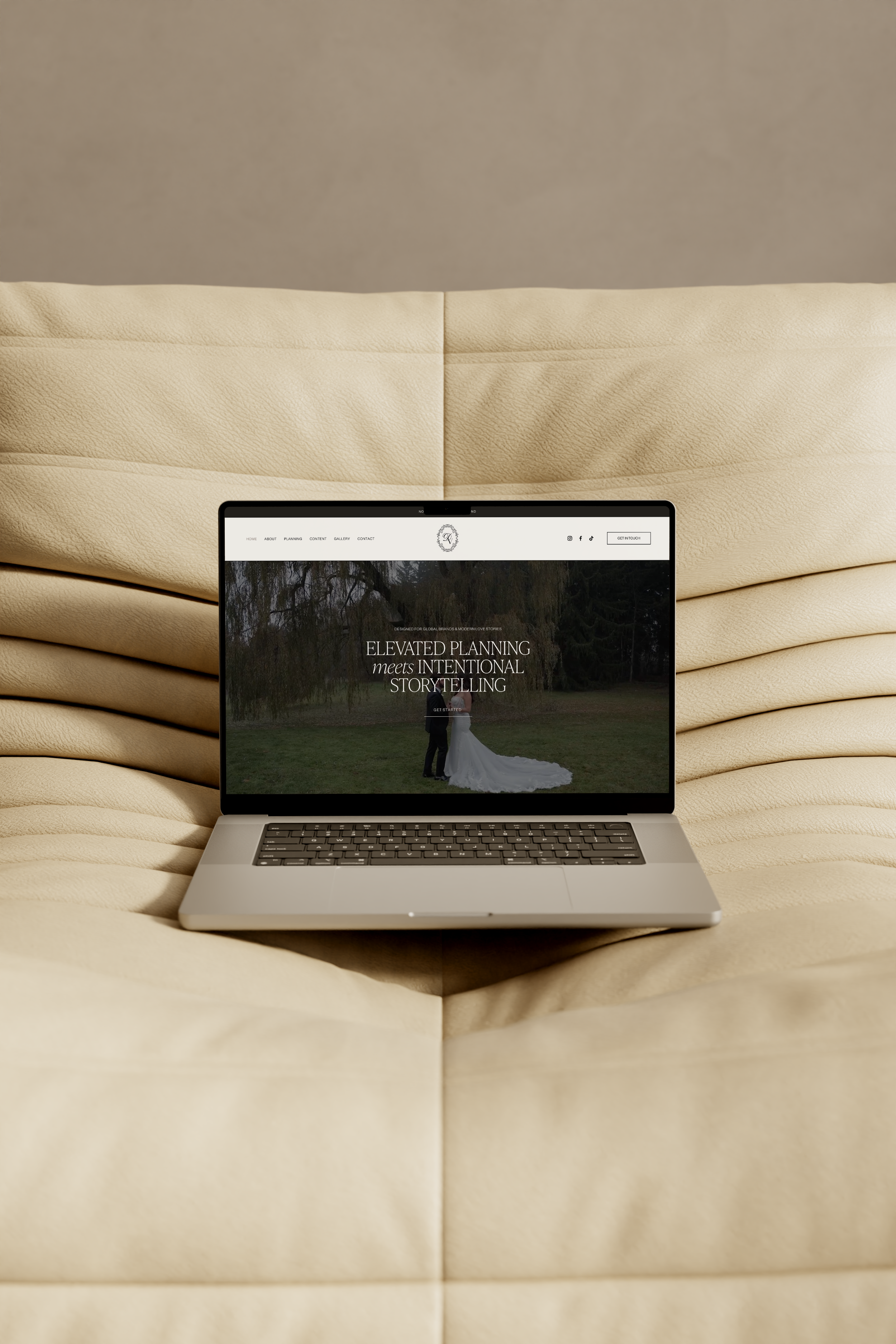 Laptop on a beige, textured cushioned surface displaying a website with a nature background and the text 'Elevated planning meets intentional storytelling.'