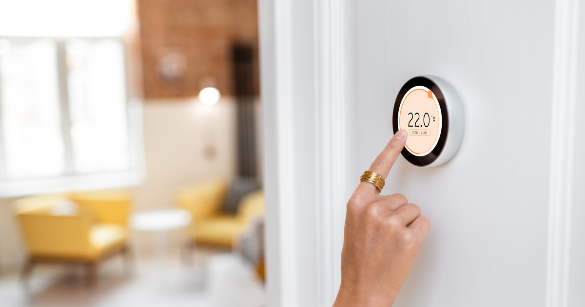 Person adjusting a wall-mounted digital thermostat displaying 22°C.