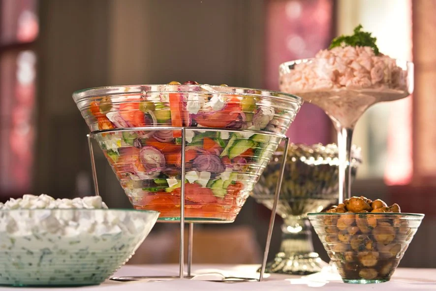 Sekoitus erilaisia salaatitölkkejä ja marinoituja oliiveja tarjoilupöydässä.