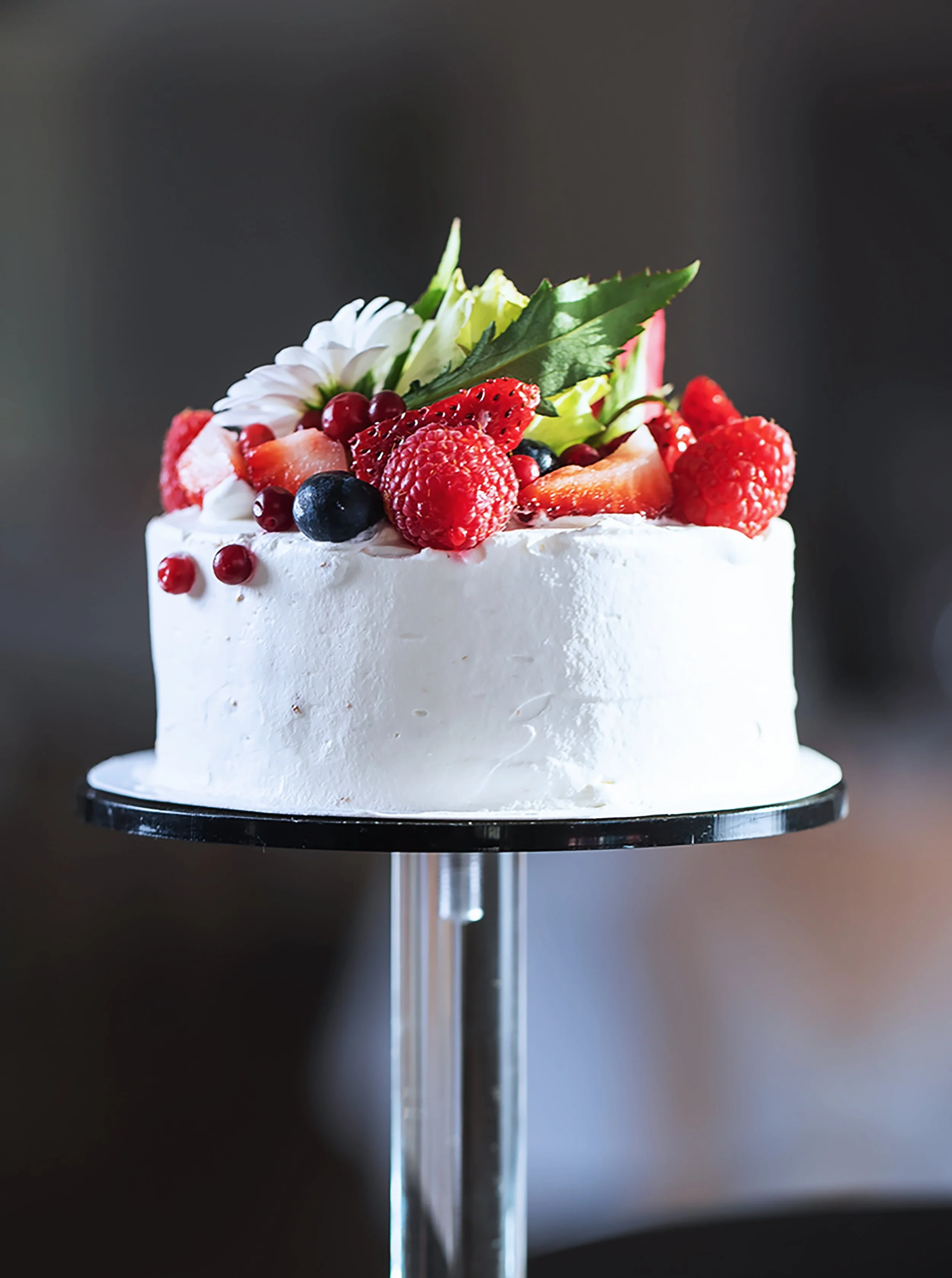 Kakku päällystetty valkoisella kuorrutteella, koristeltu tuoreilla marjoilla ja vihreällä lehdellä.