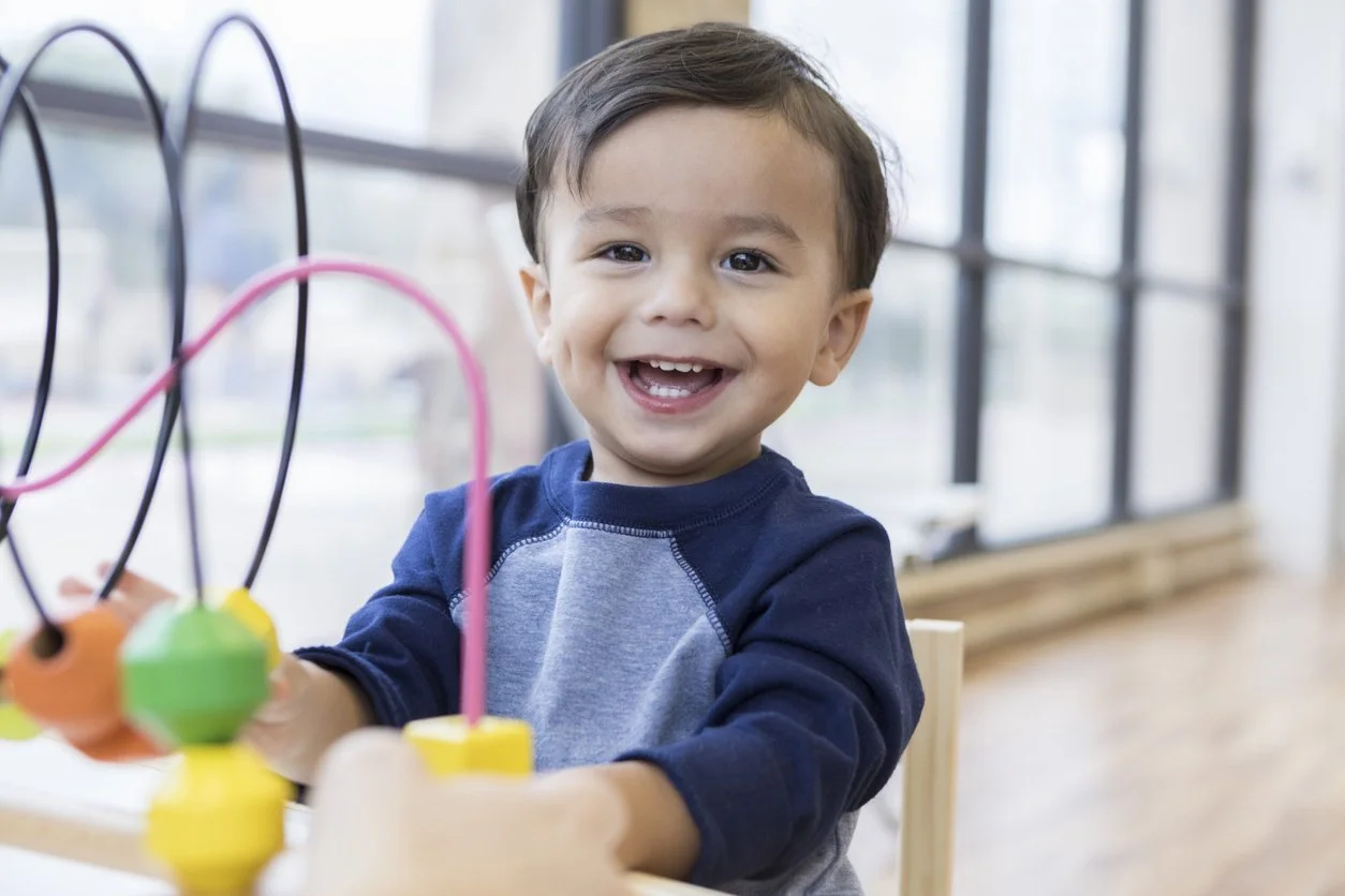 A young boy smiling while playing with a colorful bead maze toy and working on fine motor skills during occupational therapy for children in Houston, TX.