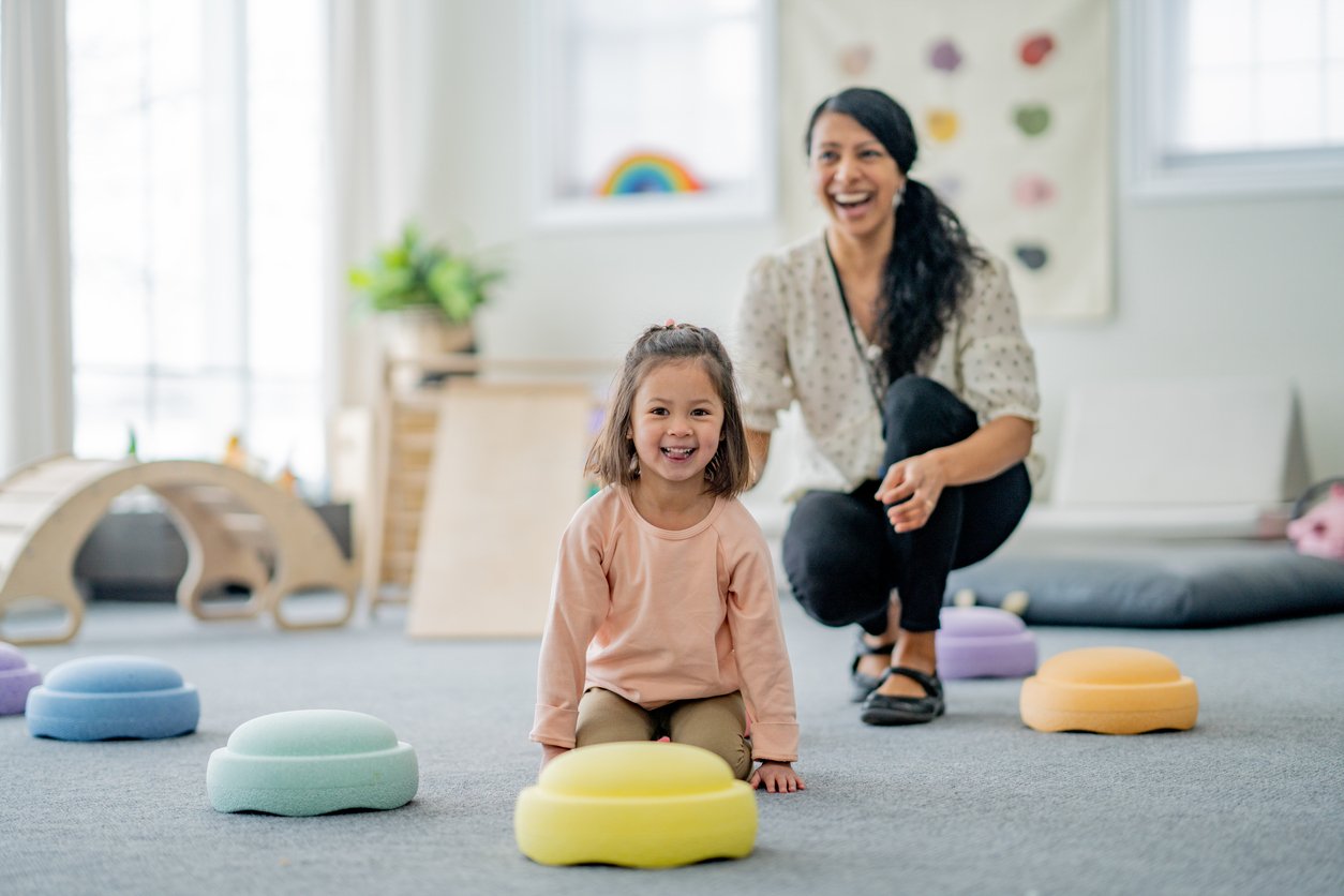 A young girl working on motor and sensory skills with an OT in a playroom with colorful cushions during occupational therapy for kids in Houston, TX.