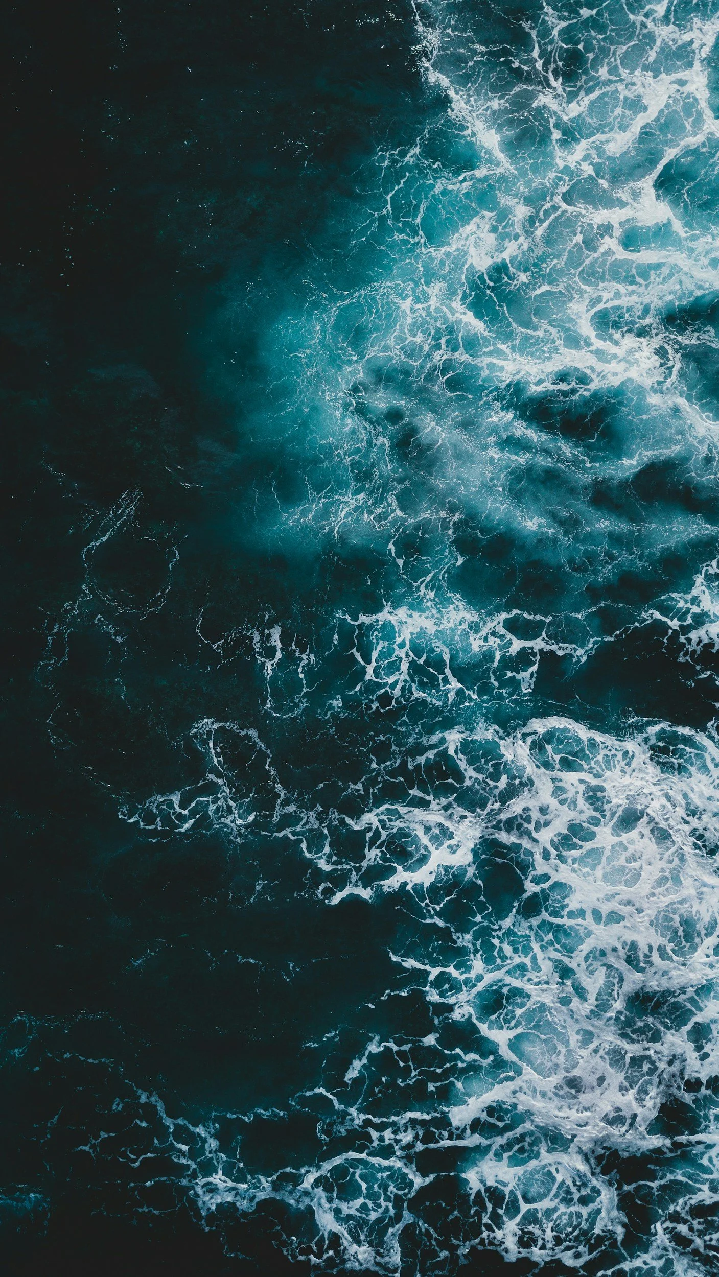 Aerial view of ocean waves with white foam and dark blue water.