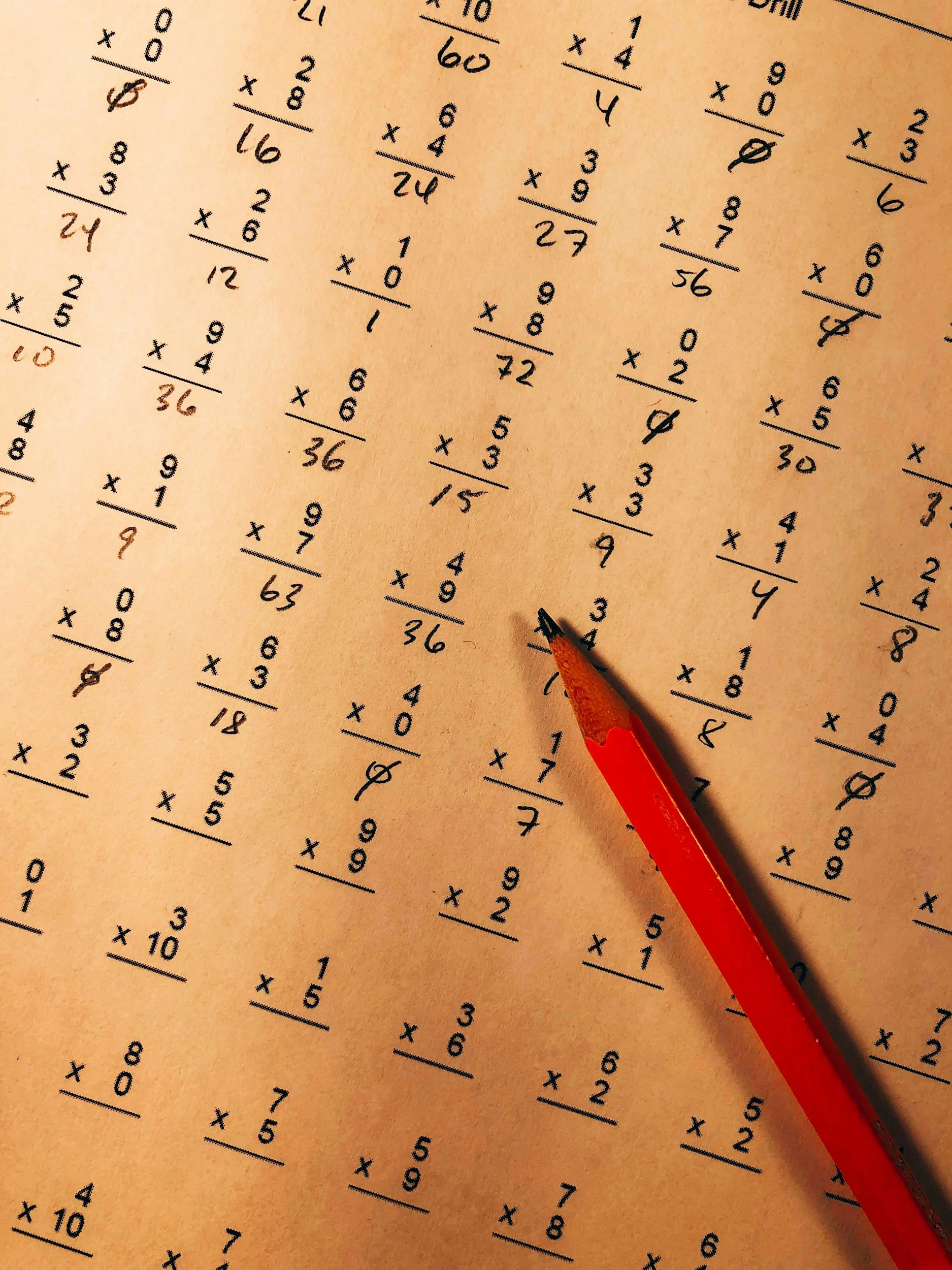 A sheet of paper filled with addition problems in black ink, and an orange pencil pointing towards one of the problems.