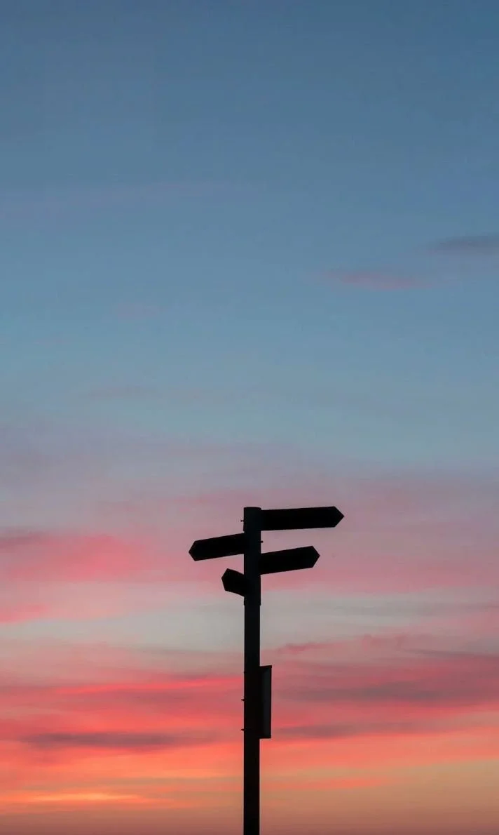 Panneau indicateur en silhouette devant un ciel au coucher du soleil avec des couleurs pastel.