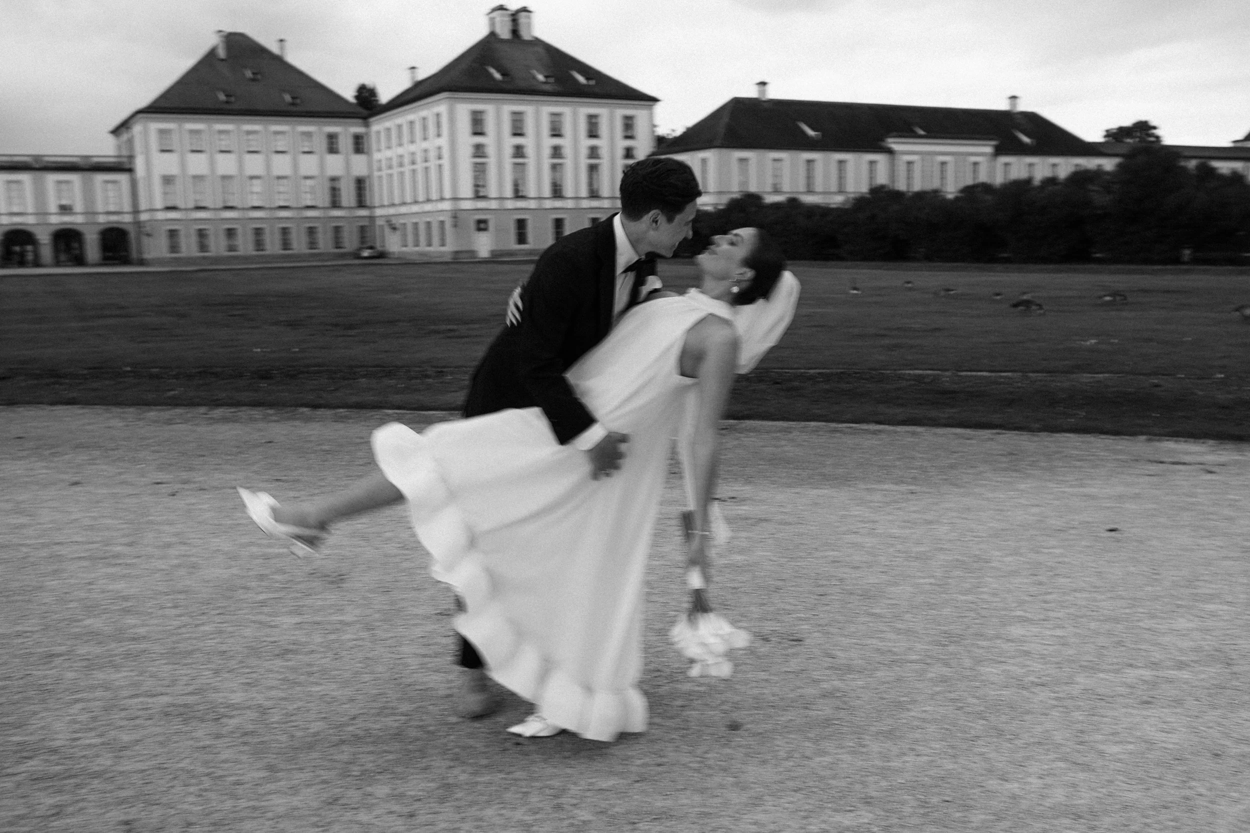 Ein schenkendes Paar tanzt im Freien vor einem historischen Gebäude, schwarz-weiß Foto.