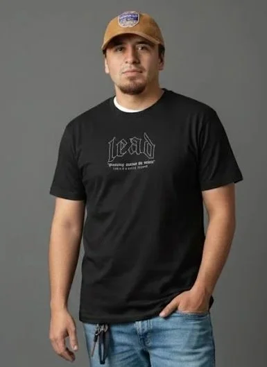 A young man wearing a brown baseball cap and a black T-shirt with the word 'head' printed on it, standing against a gray background.