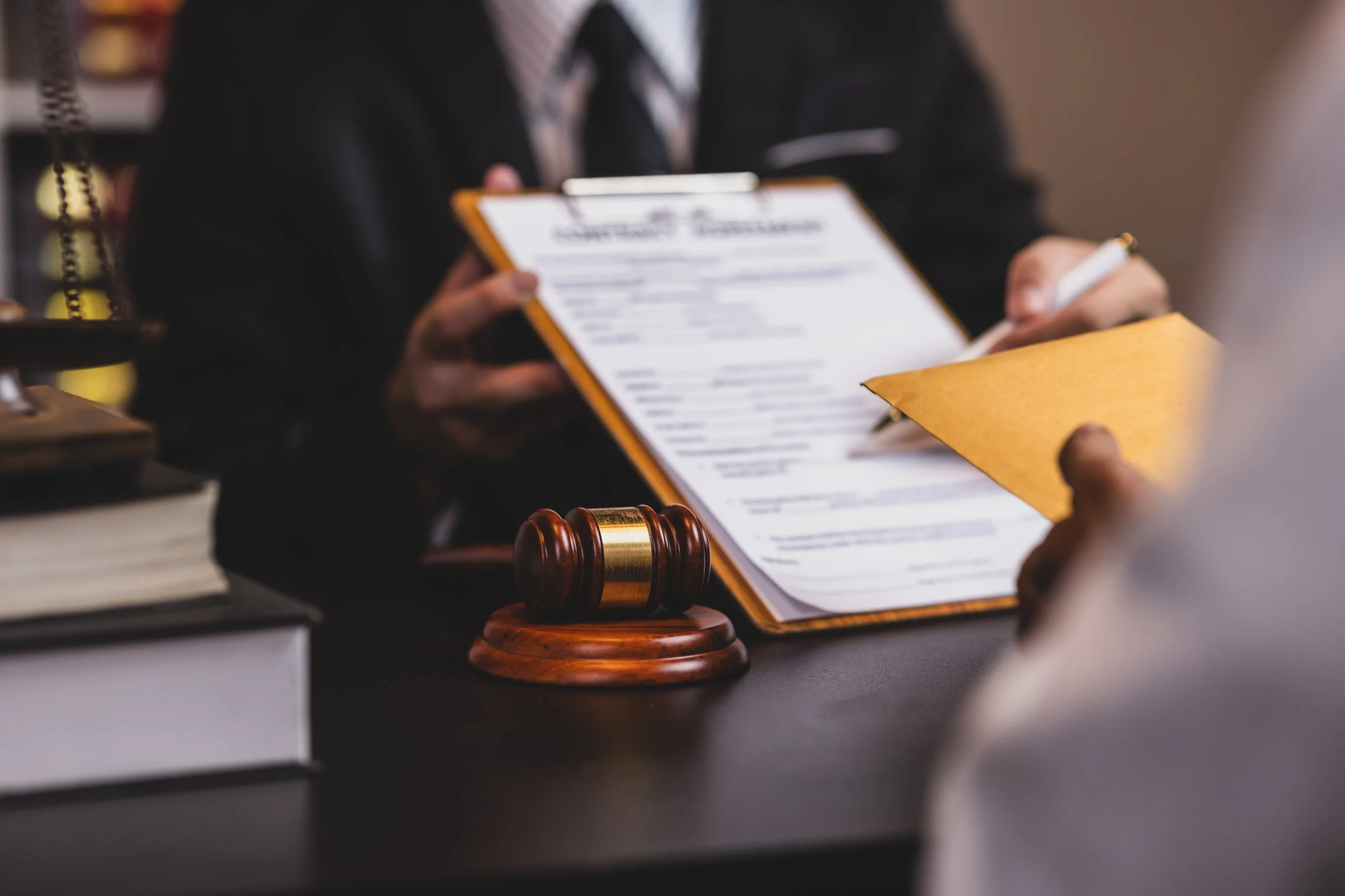 Close-up of a legal professional or judge in a courtroom, holding a clipboard with a document, with a gavel on the desk in front.