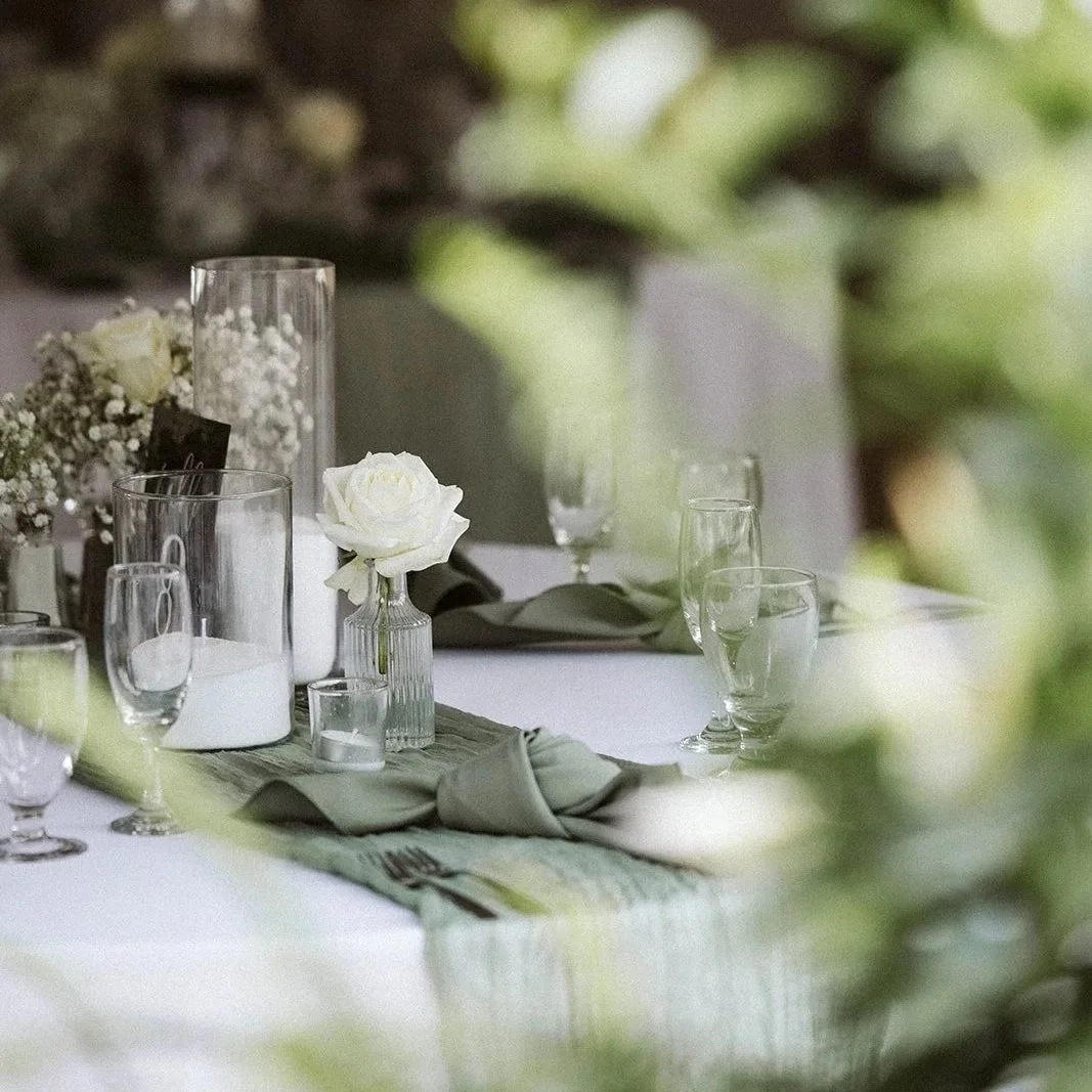 Elegant table setting with glassware, white flowers, candles, and gray napkins on a table with a white tablecloth, decorated for a formal event.