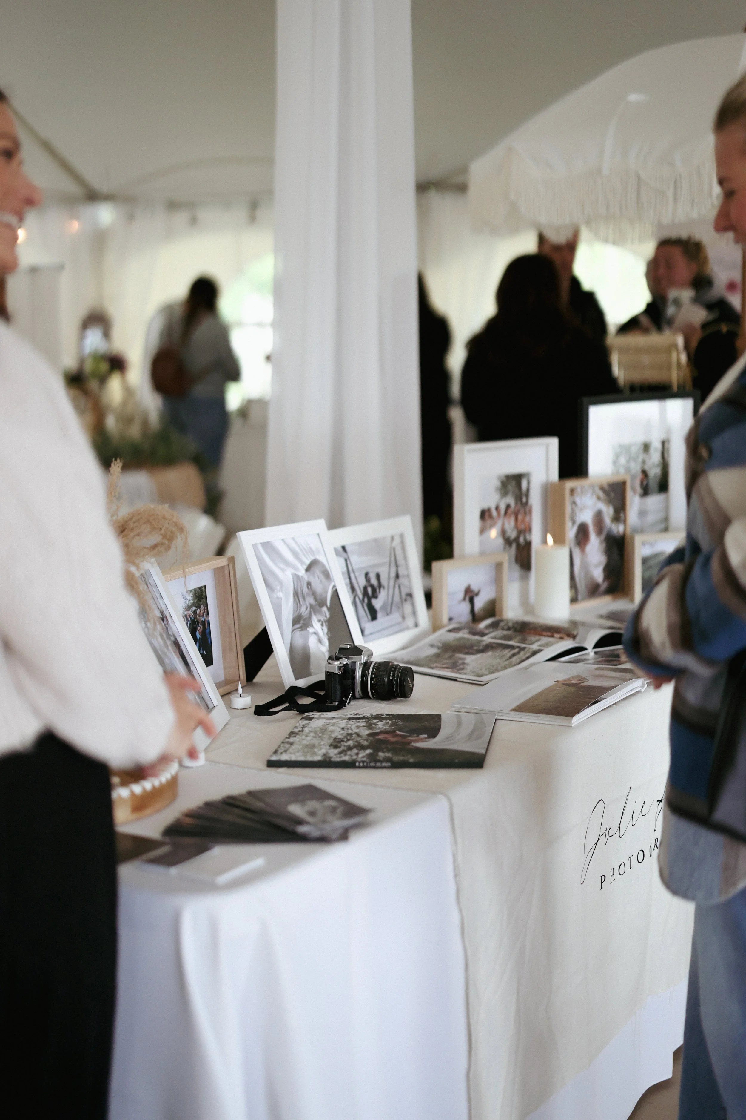 Display table with framed photographs, a camera, and printed materials at a photography booth during a wedding event.