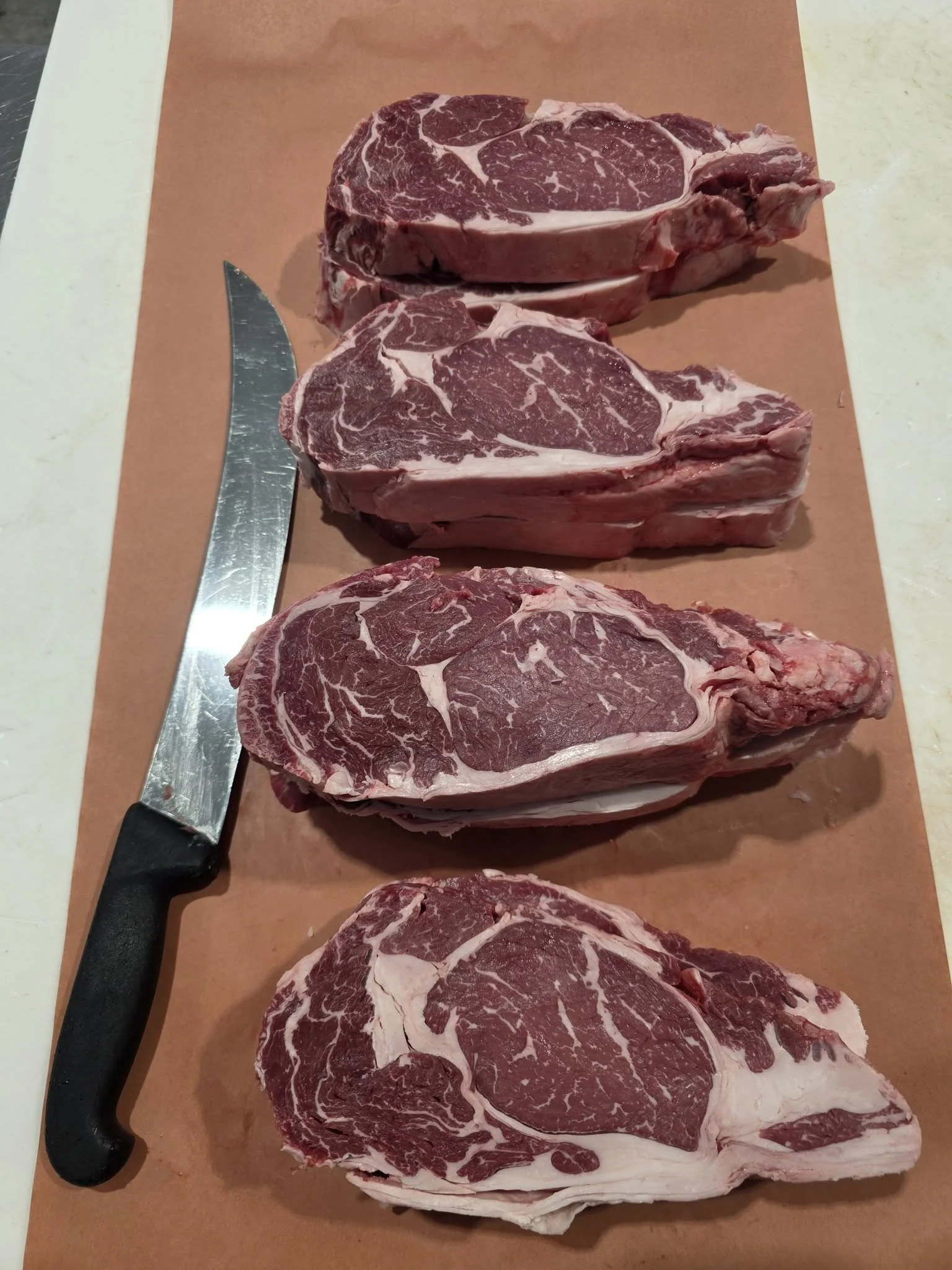 Four raw beef chuck steaks on a cutting board with a kitchen knife.
