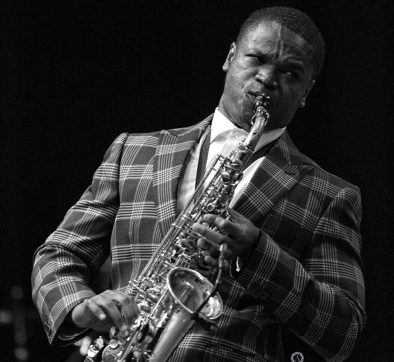 Langston Hughes II; Black and white photo of a man playing a saxophone, wearing a plaid suit and white shirt.