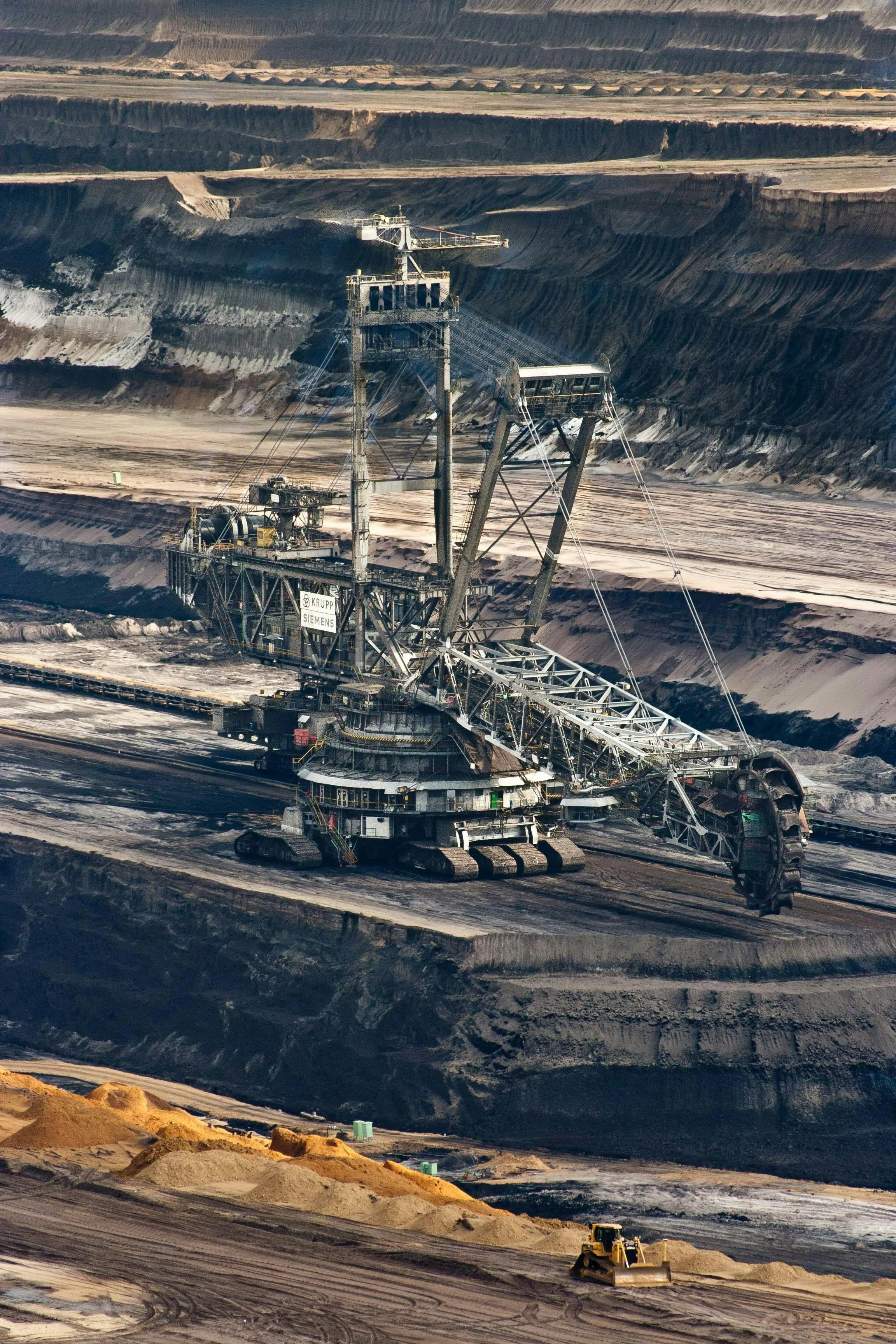 Large mining excavator in an open-pit mine with layered earth and mineral deposits.