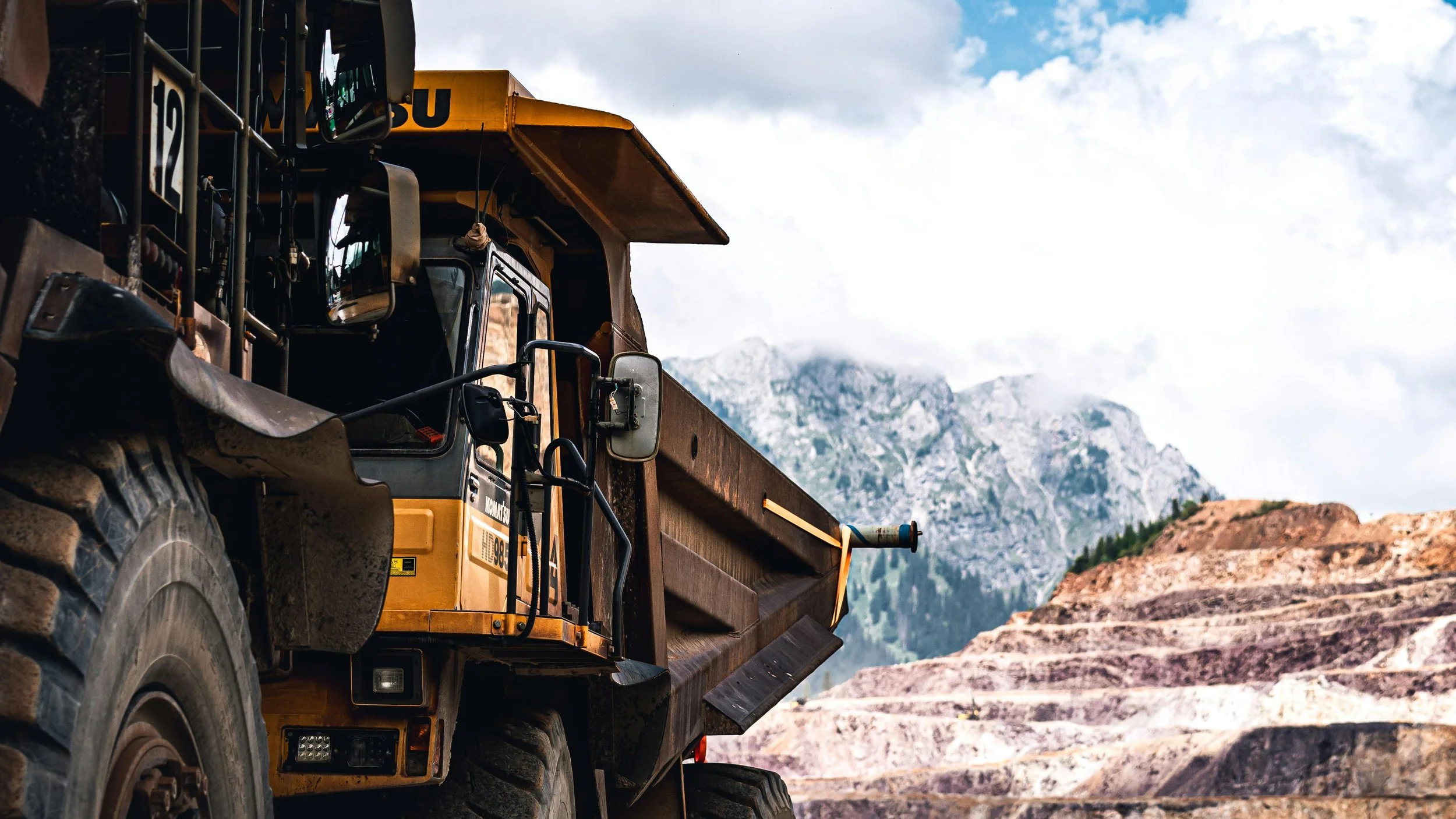 A yellow dump truck in a quarry with mountain ranges in the background.
