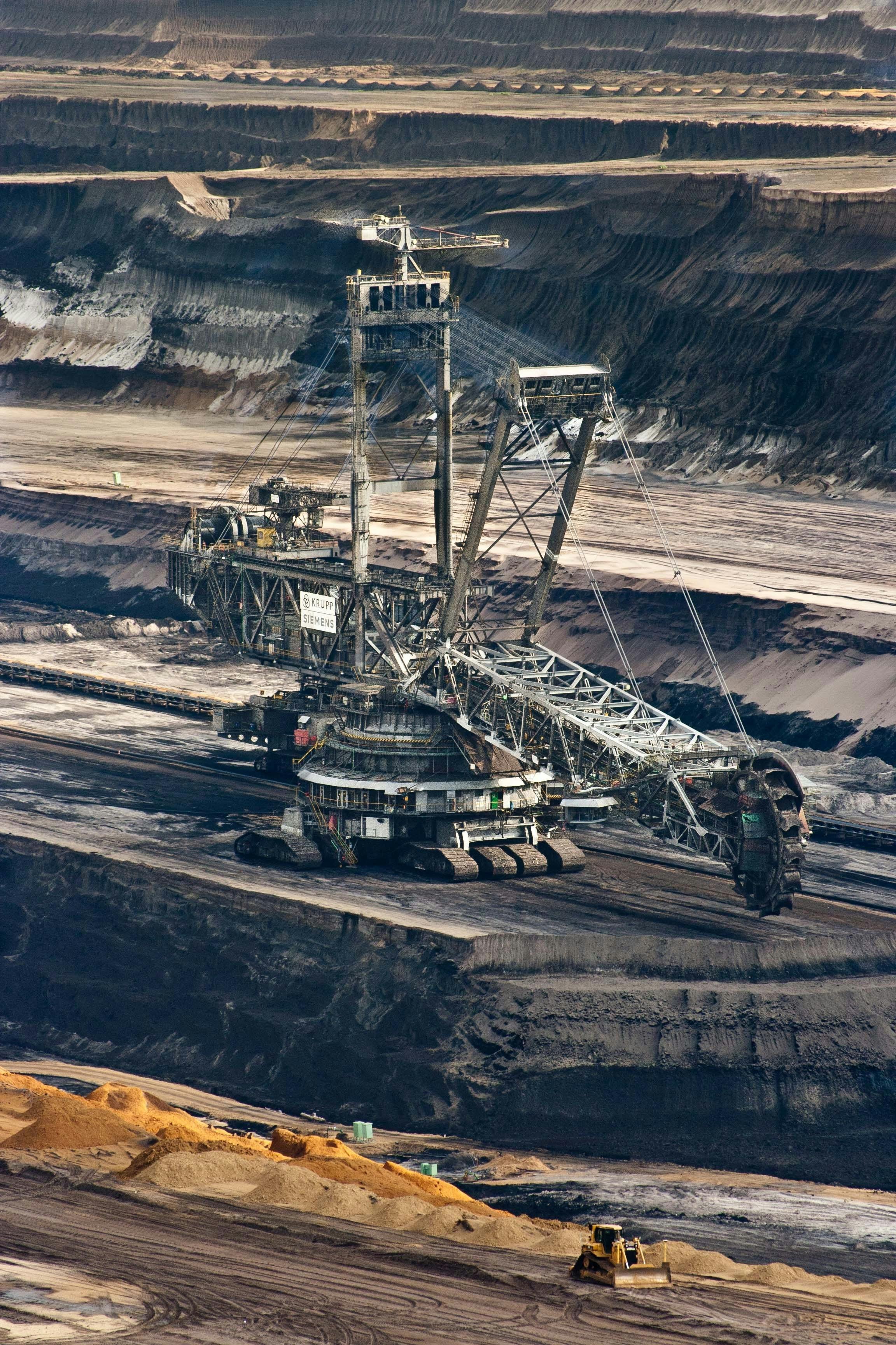 A large open-pit mining dragline excavator working in a quarry with terraced soil and rock layers.