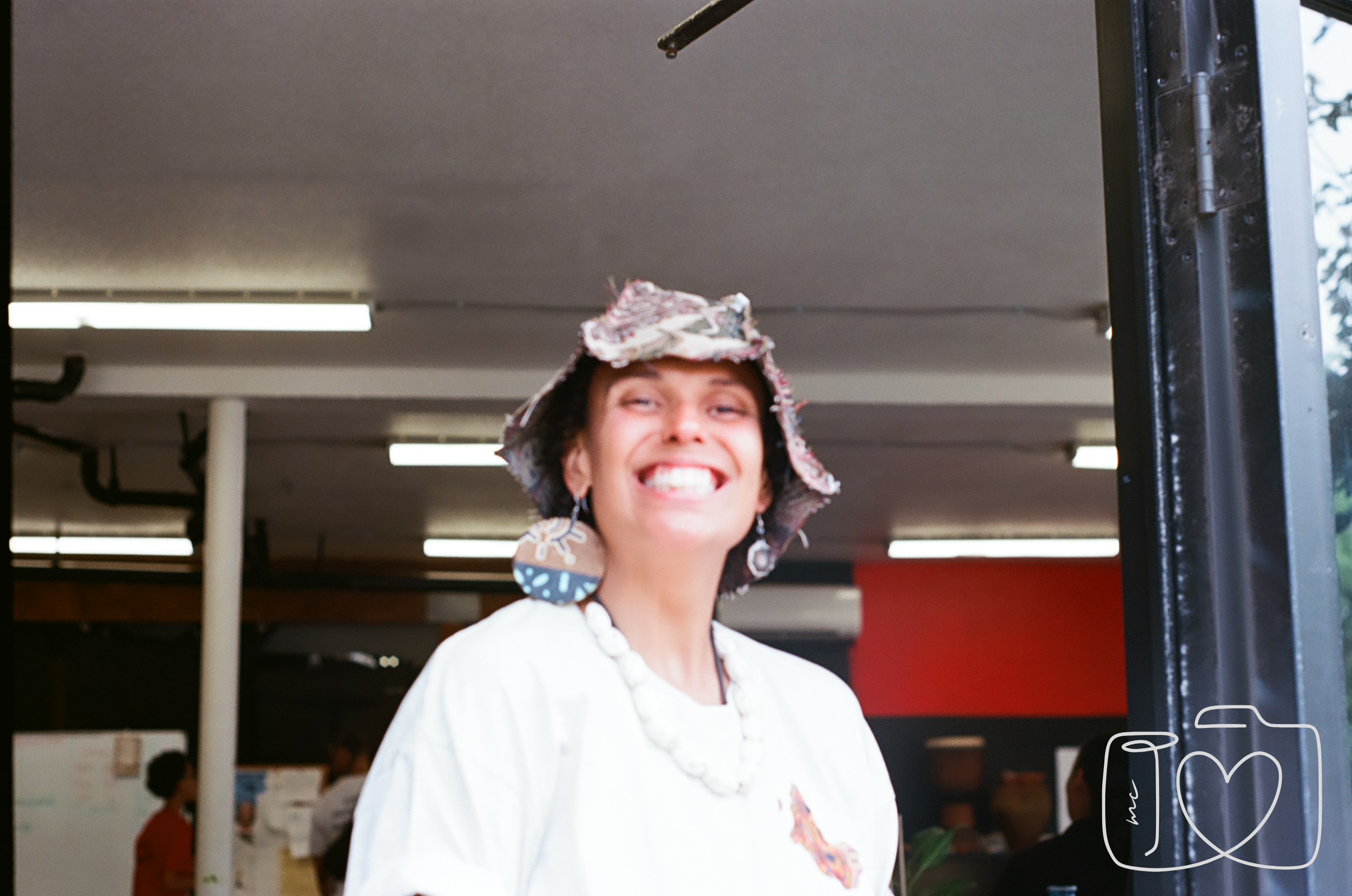 Woman smiling, wearing a colorful hat, large earrings, and a necklace inside a building.
