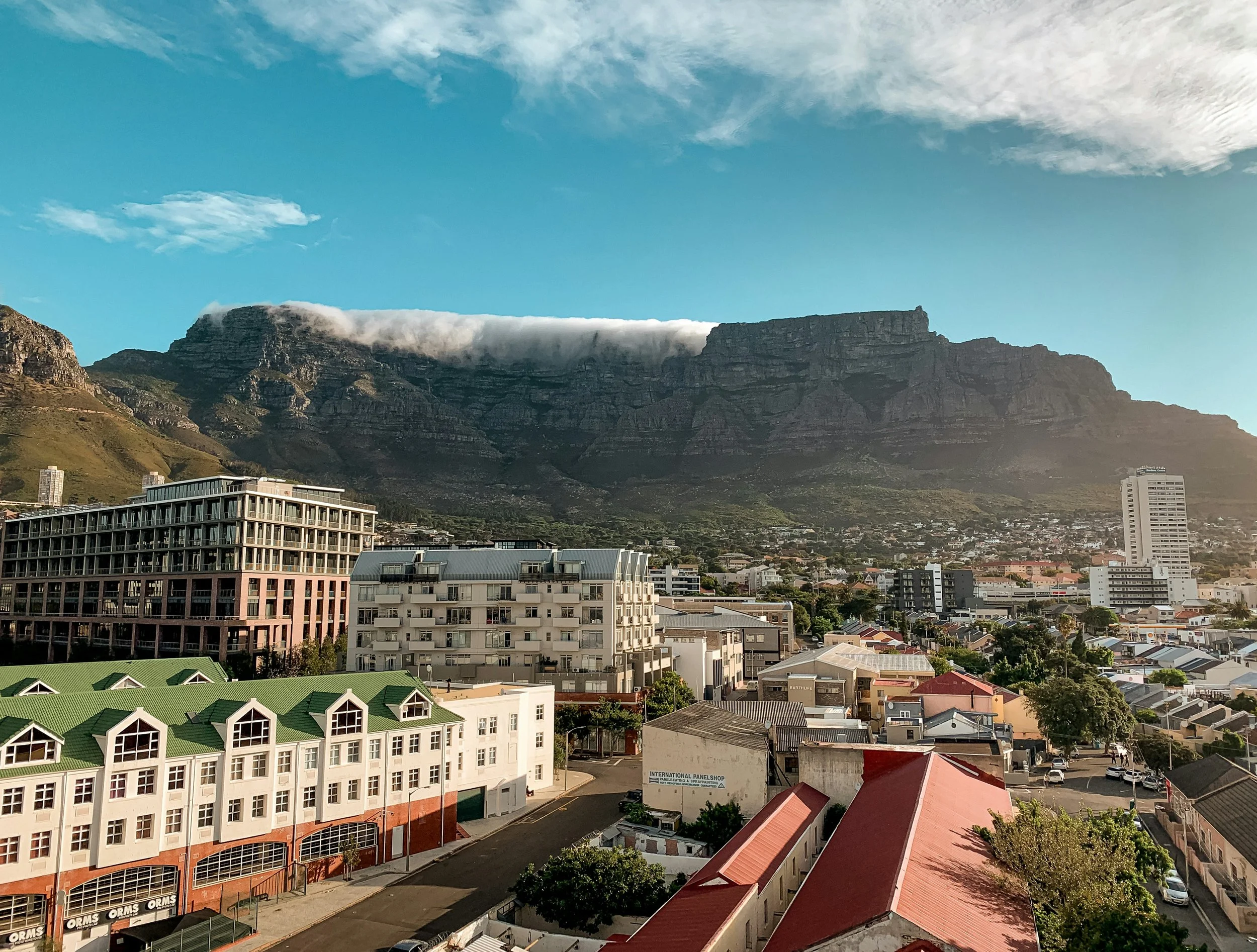 Cityscape with various buildings in front of a mountain with a flat top, under a partly cloudy sky.