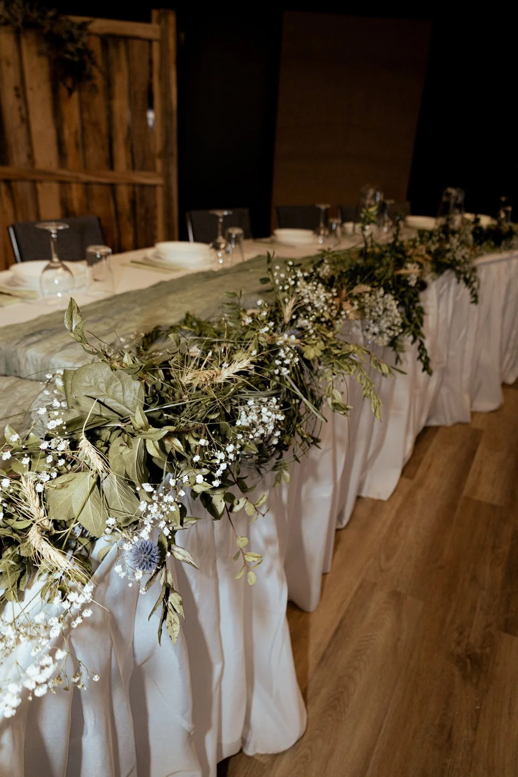 Reception decor at Open Country Farm wedding venue in Alberta. Head table lined with beautiful greenery. Indoor seating up to 120 guests near Calgary Alberta