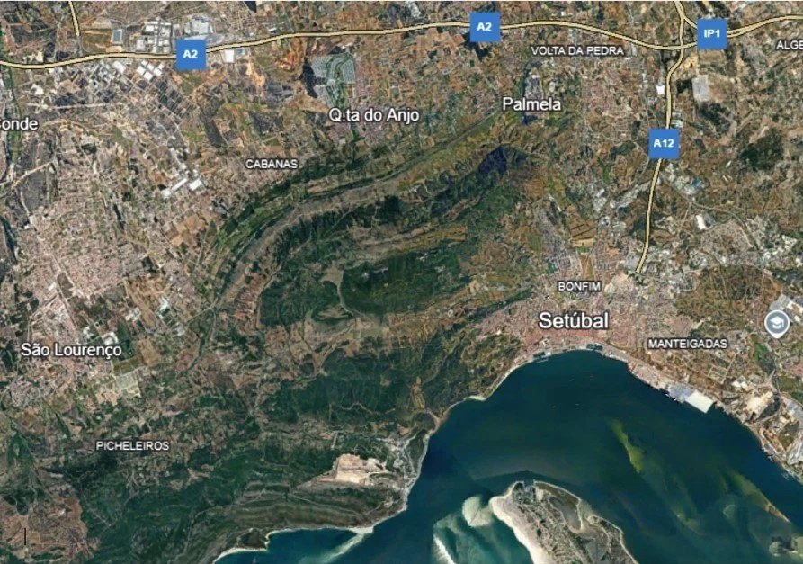 An aerial satellite view of Setúbal, Portugal, showing the coastline, river, and surrounding neighborhoods and roads.