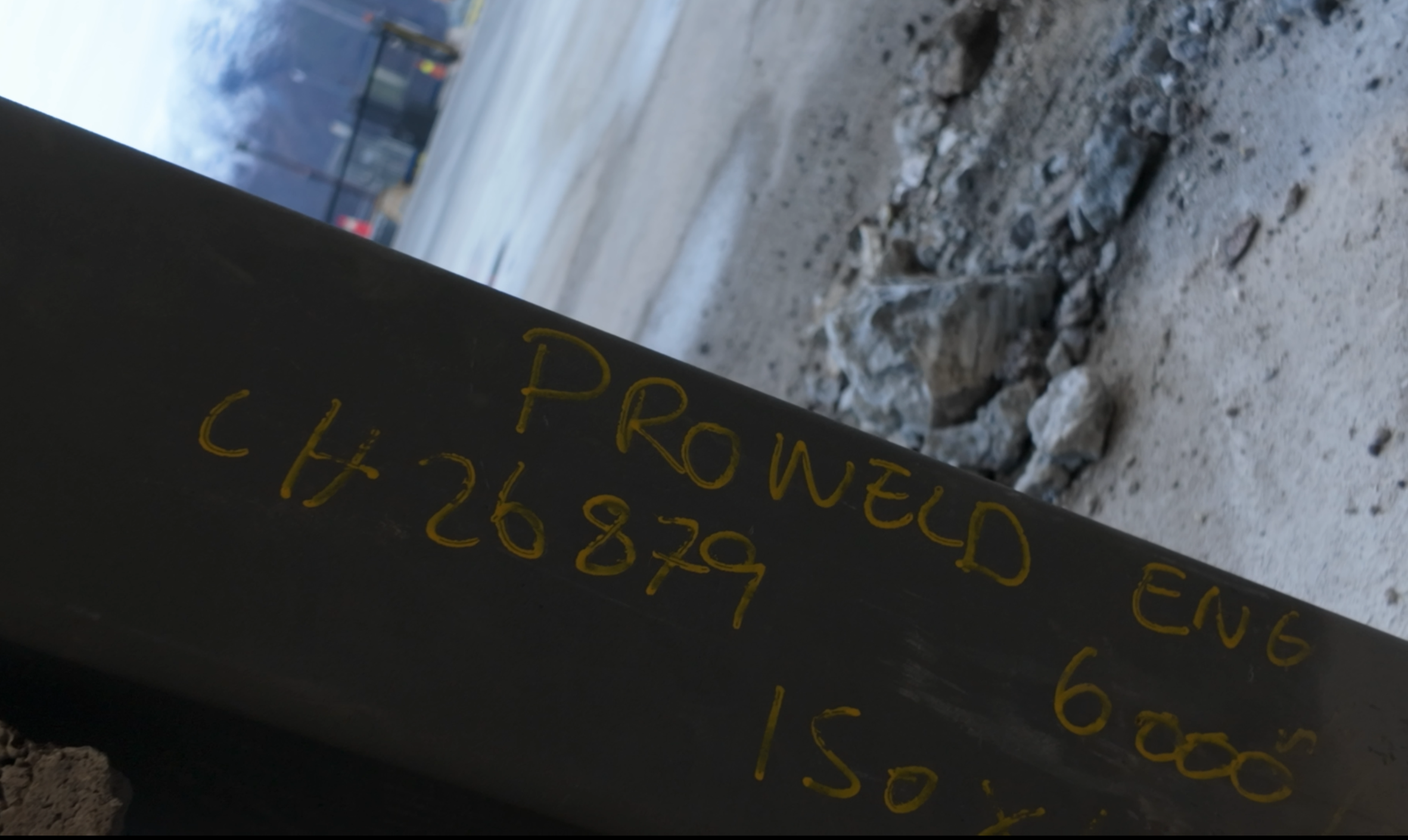 En svart stolpe med gulkode skrevet på den, og en byggeplass med jord, stein og en bygning i bakgrunnen.