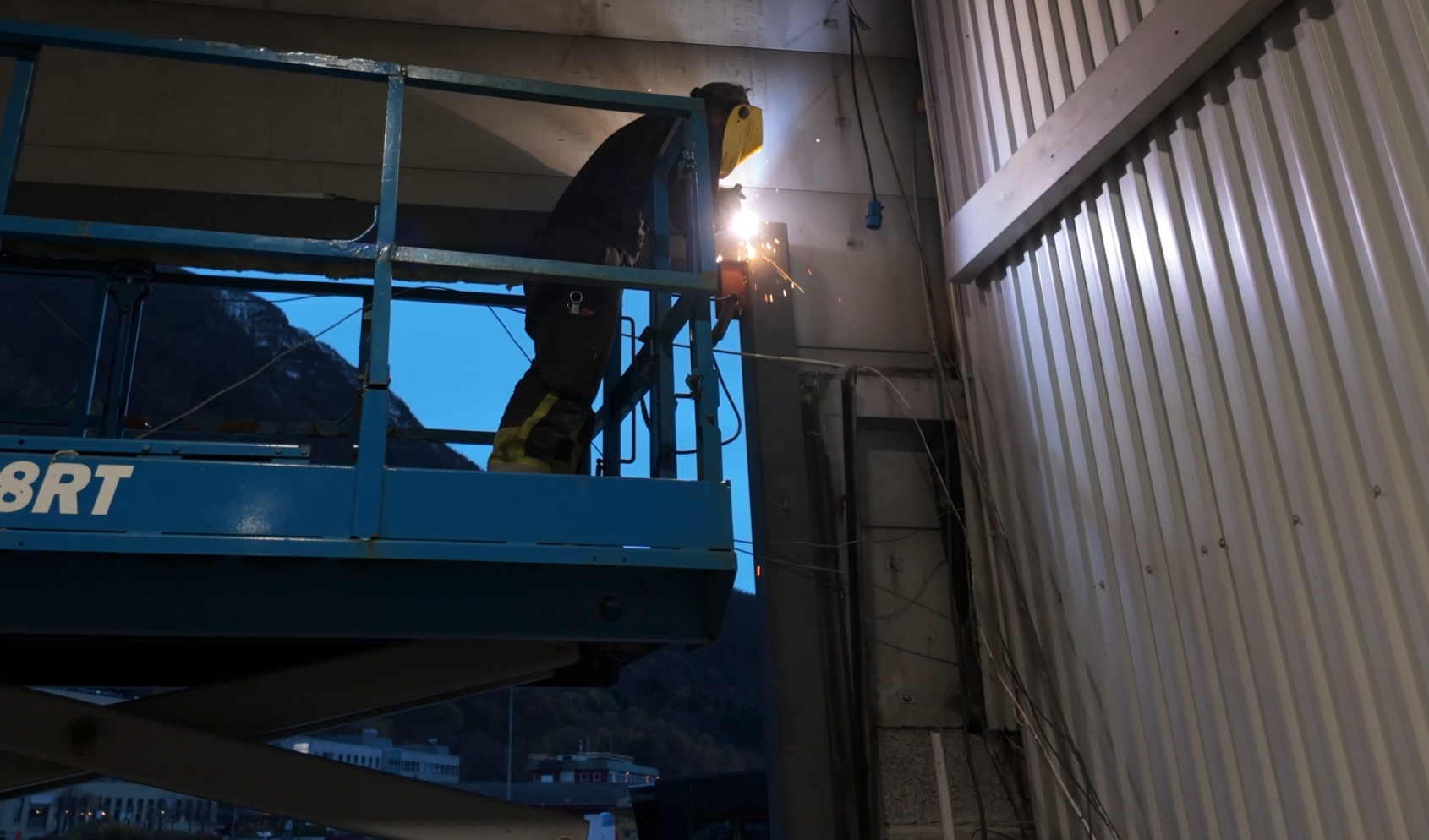 En person som bruker verneutstyr og sveiser på en platform inne i et bygg.