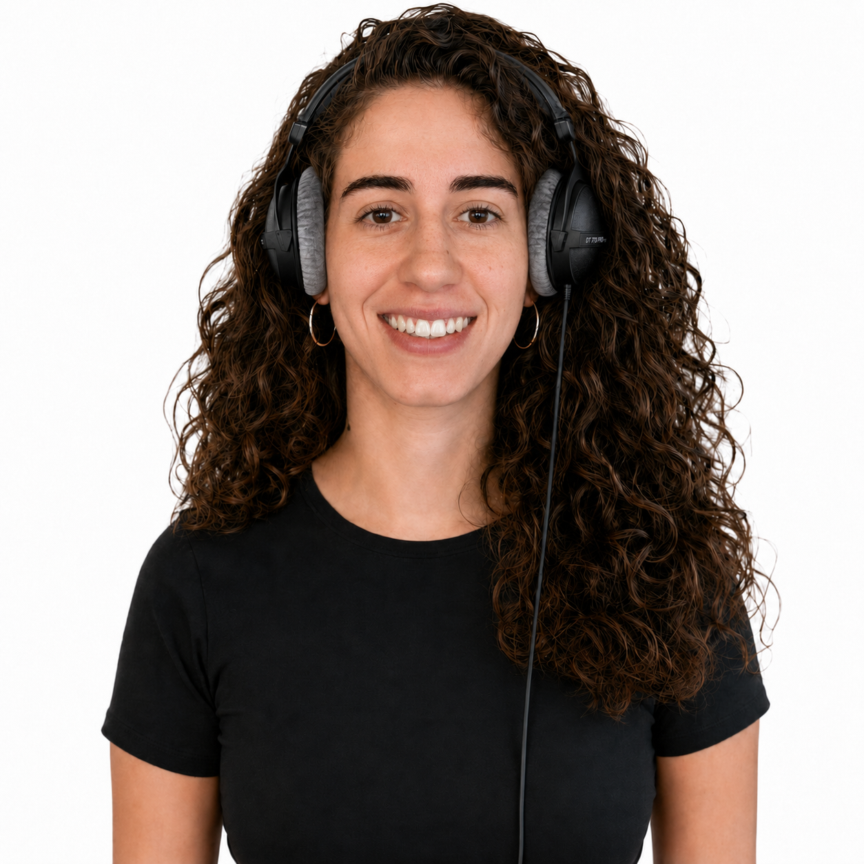 Joven mujer con cabello rizado, usando auriculares y camiseta negra, sonriendo frente a fondo blanco.