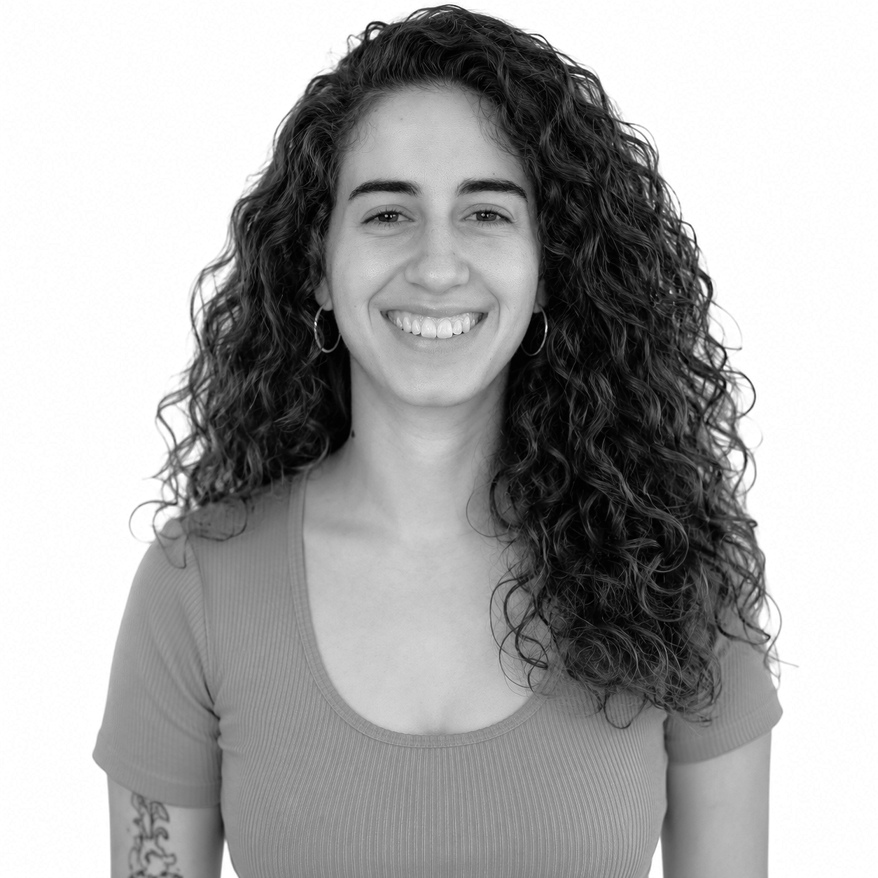 Retrato en blanco y negro de una mujer con rizos largos y oscuros, sonriendo, usando una camiseta de manga corta