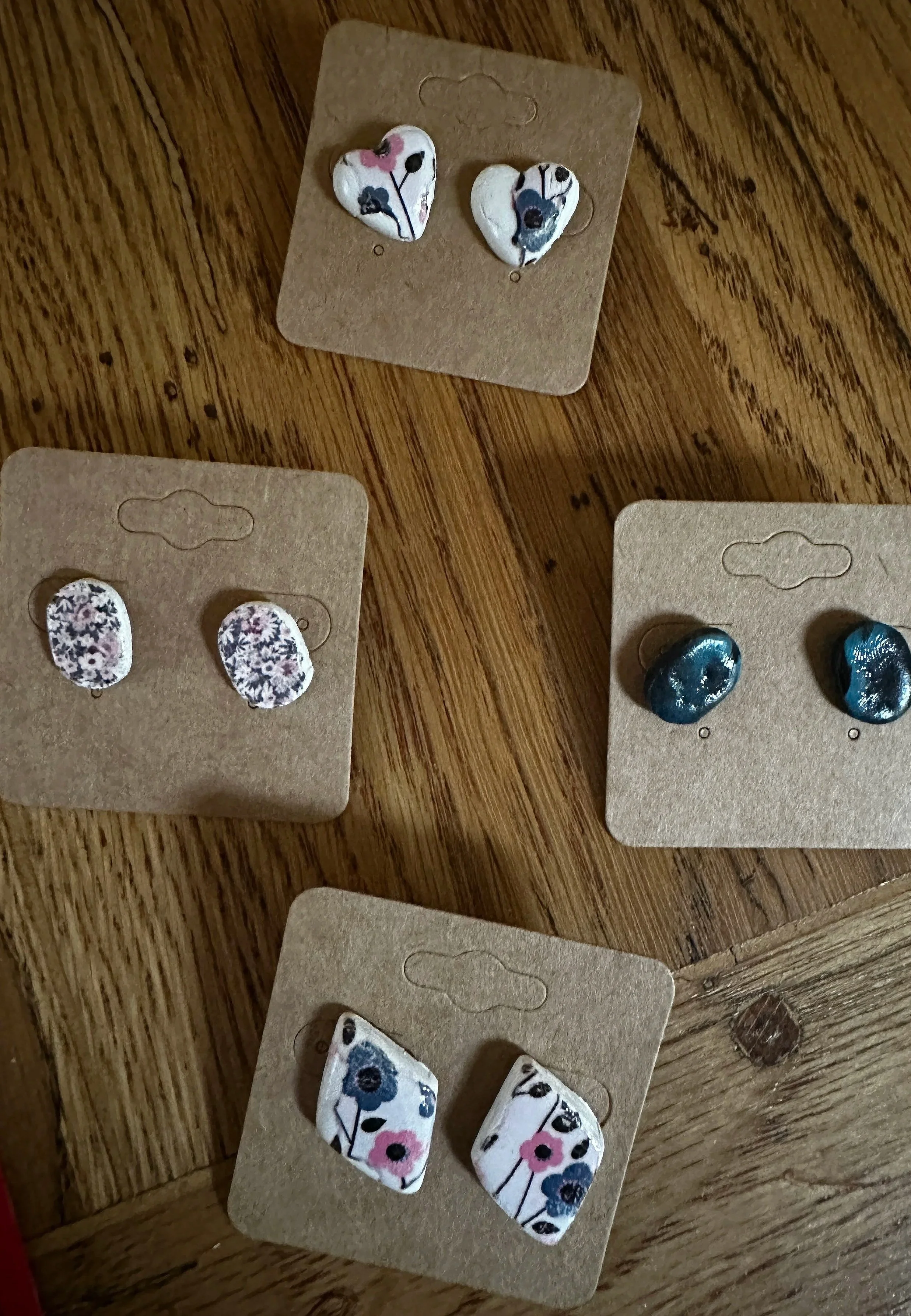 Four pairs of floral-patterned earrings displayed on cardboard cards on a wooden surface.